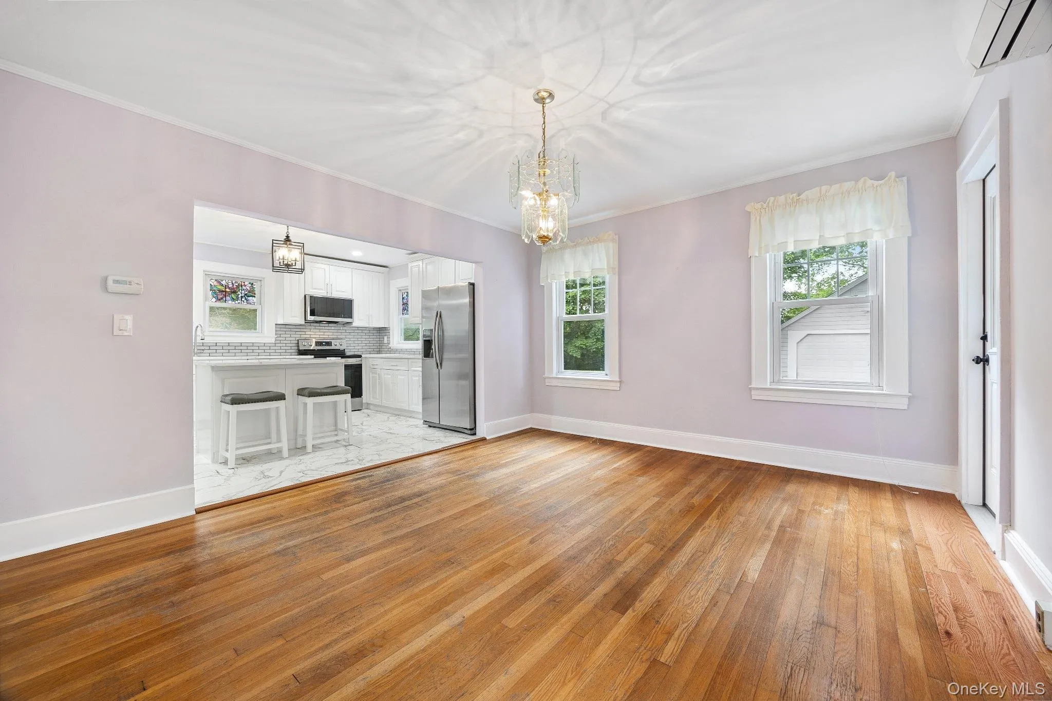 Unfurnished living room featuring light wood-style flooring, crown molding, a chandelier, and a wall mounted AC Unfurnished living room featuring light wood-style flooring, crown molding, a chandelier, and a wall mounted AC