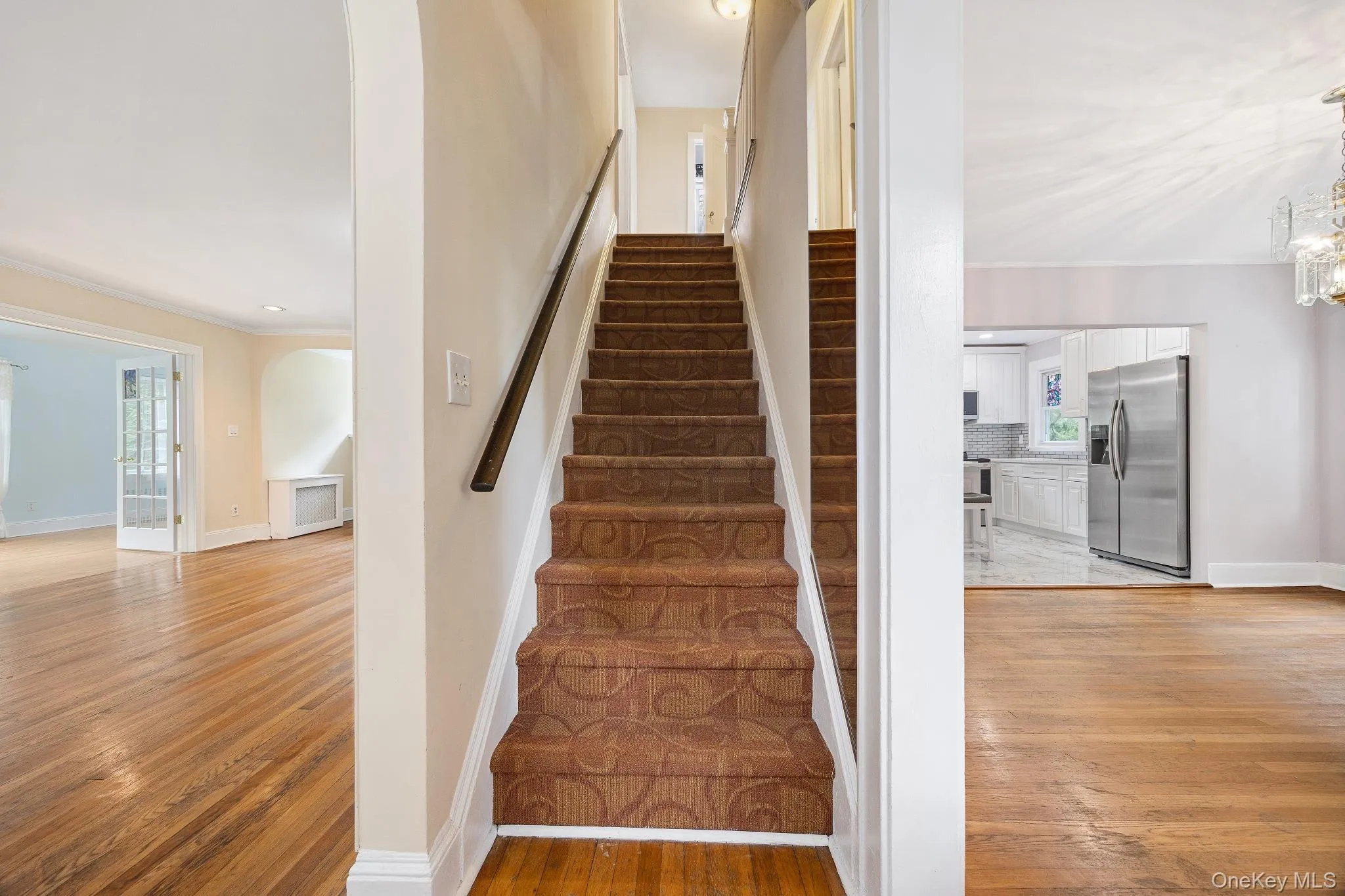Staircase featuring arched walkways, crown molding, wood finished floors, and a chandelier Staircase featuring arched walkways, crown molding, wood finished floors, and a chandelier