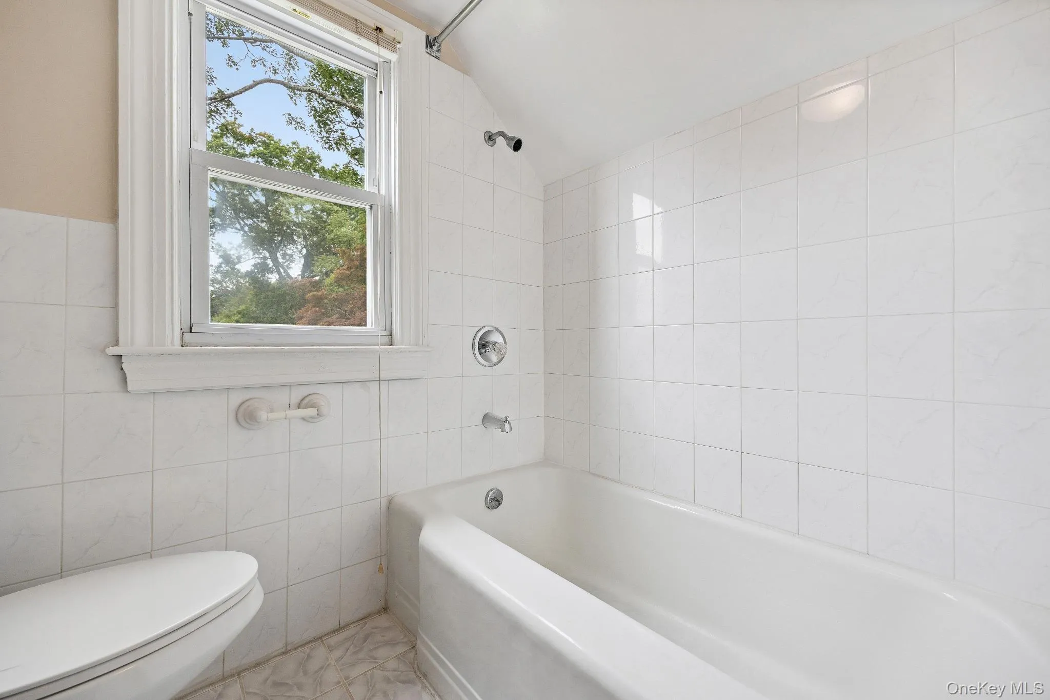 Full bath with tile walls, vaulted ceiling, and bathing tub / shower combination Full bath with tile walls, vaulted ceiling, and bathing tub / shower combination