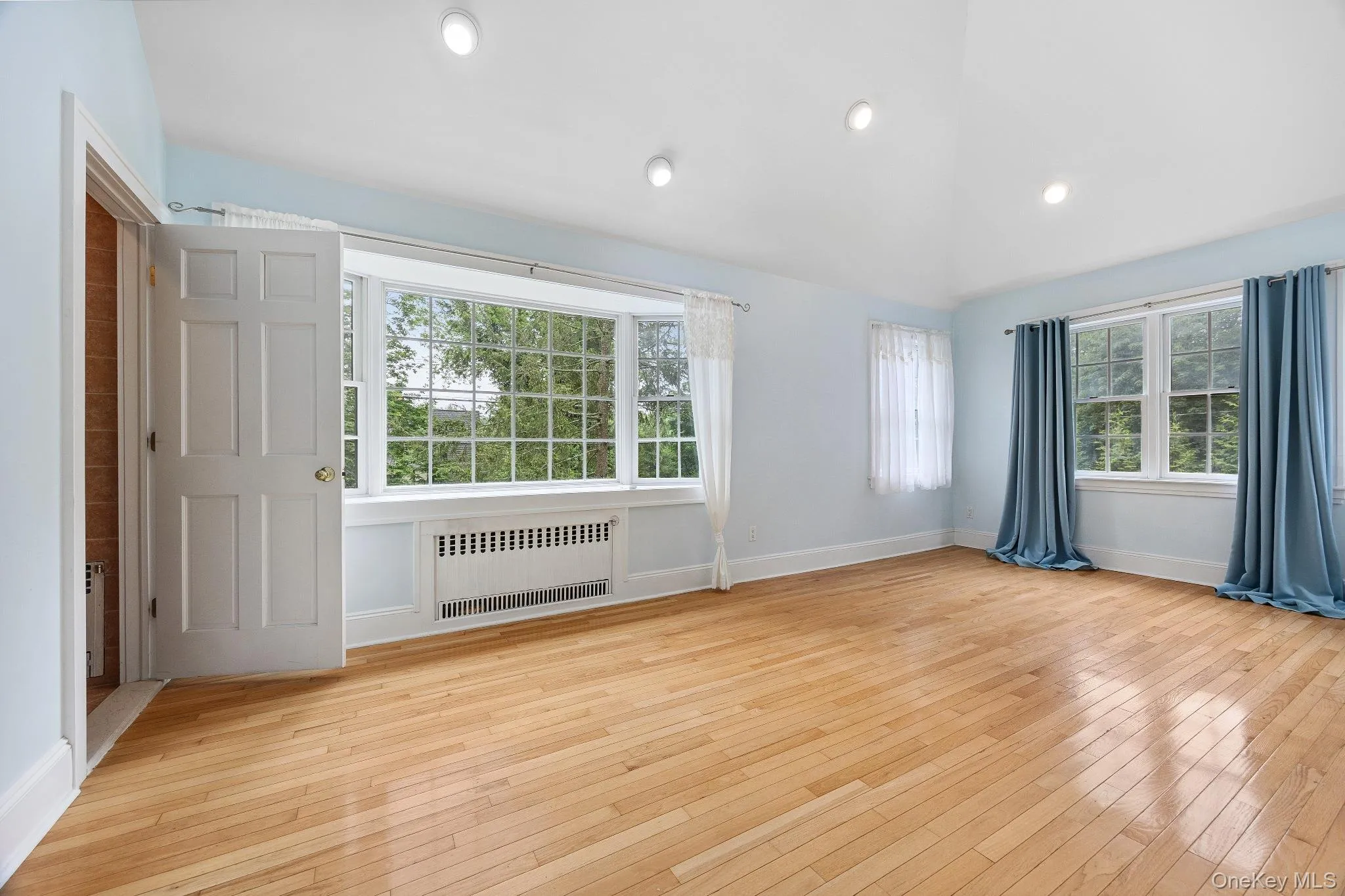 Spare room featuring radiator heating unit, healthy amount of natural light, hardwood / wood-style floors, lofted ceiling, and recessed lighting Spare room featuring radiator heating unit, healthy amount of natural light, hardwood / wood-style floors, lofted ceiling, and recessed lighting