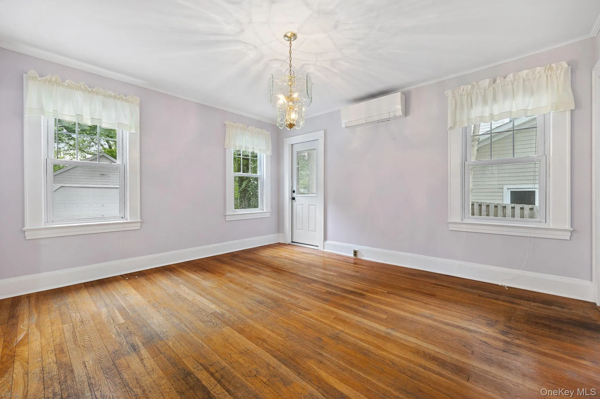 Spare room with an AC wall unit, a chandelier, plenty of natural light, hardwood / wood-style floors, and crown molding Spare room with an AC wall unit, a chandelier, plenty of natural light, hardwood / wood-style floors, and crown molding