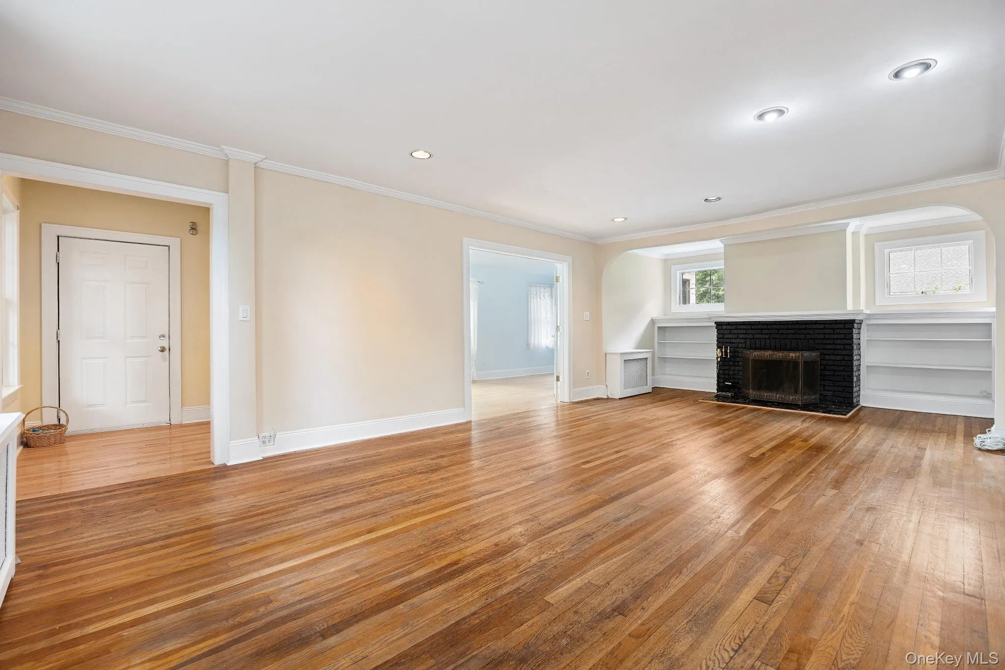 Unfurnished living room with light wood-style flooring, ornamental molding, a brick fireplace, and recessed lighting Unfurnished living room with light wood-style flooring, ornamental molding, a brick fireplace, and recessed lighting