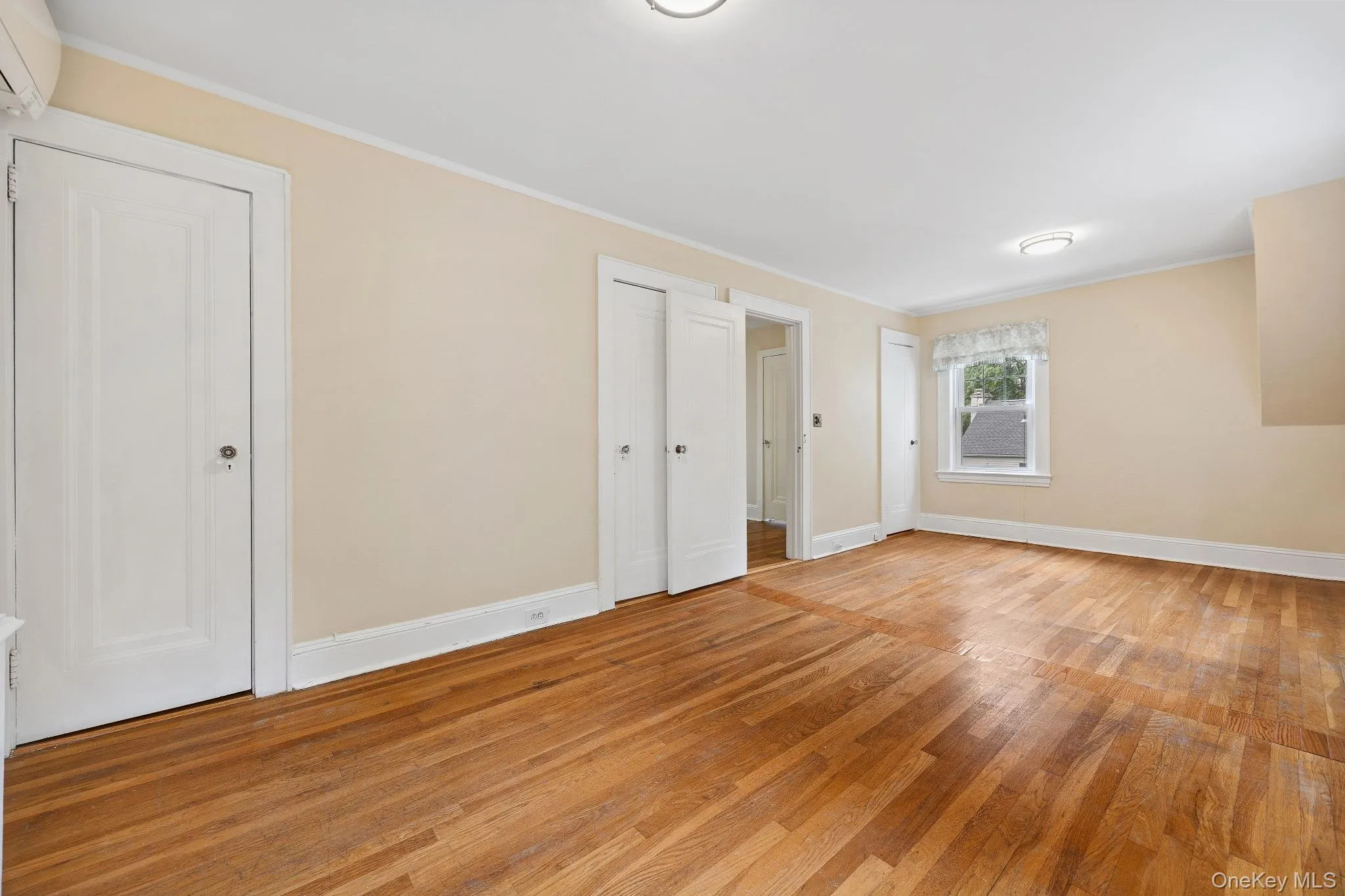 Unfurnished bedroom with light wood-style flooring, ornamental molding, a wall unit AC, and two closets Unfurnished bedroom with light wood-style flooring, ornamental molding, a wall unit AC, and two closets