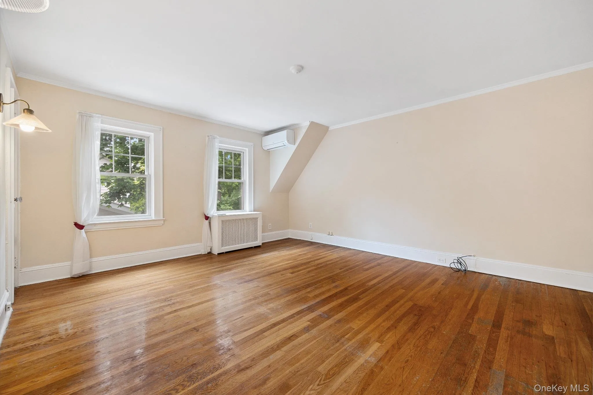 Bonus room with radiator heating unit, a wall mounted air conditioner, and wood finished floors Bonus room with radiator heating unit, a wall mounted air conditioner, and wood finished floors