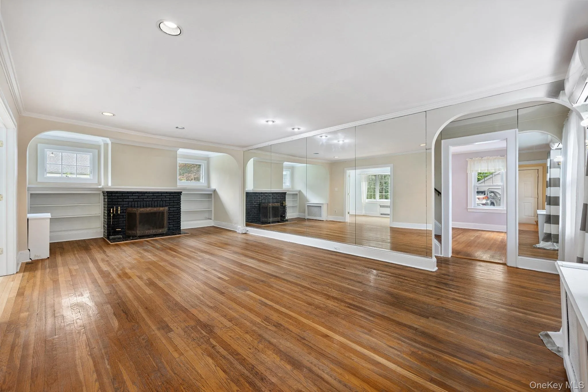 Unfurnished living room featuring a brick fireplace, arched walkways, crown molding, wood-type flooring, and recessed lighting Unfurnished living room featuring a brick fireplace, arched walkways, crown molding, wood-type flooring, and recessed lighting