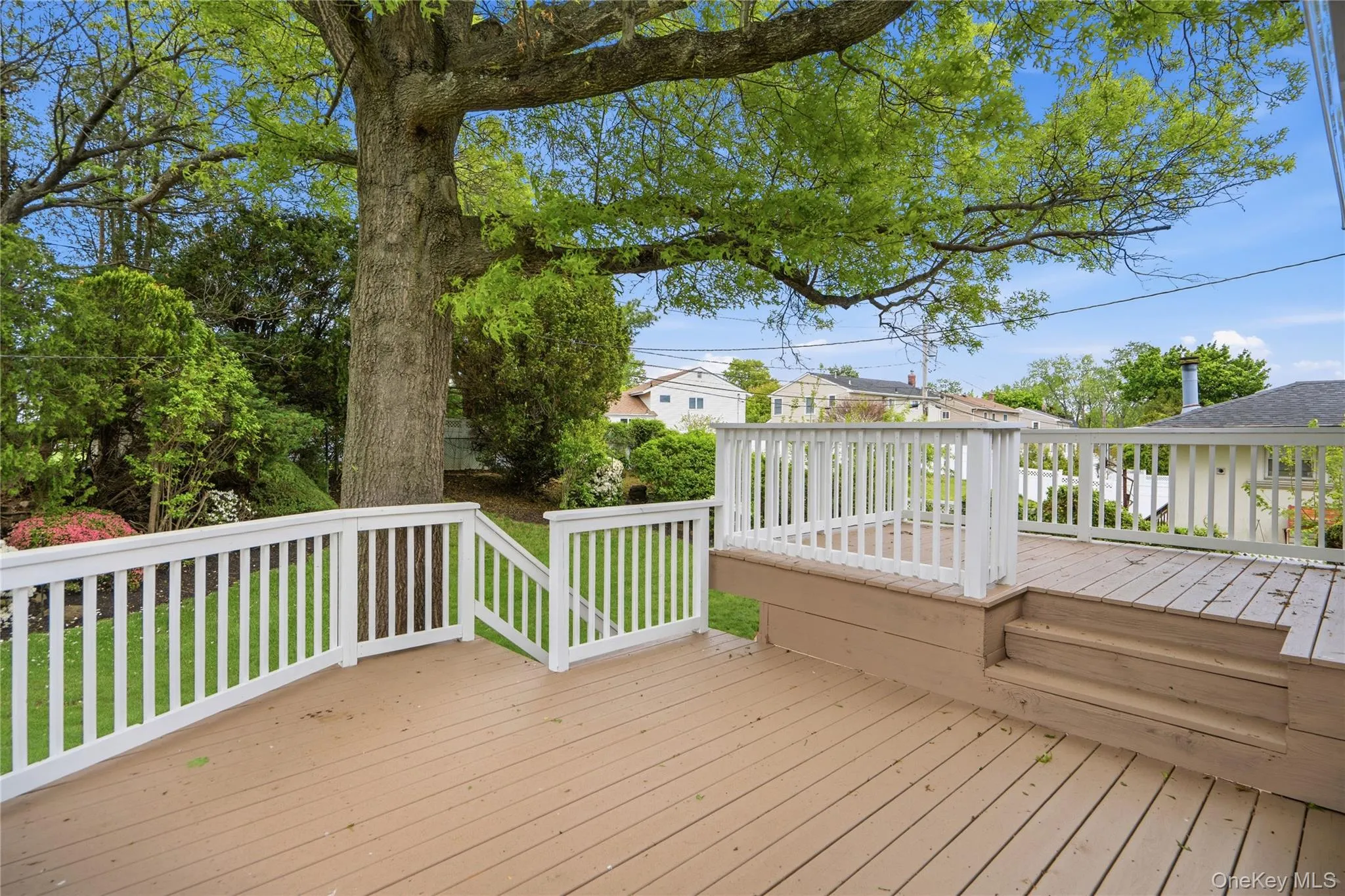 Multi-level wood-finish deck with white railings situated off the kitchen with steps to patio Multi-level wood-finish deck with white railings situated off the kitchen with steps to patio