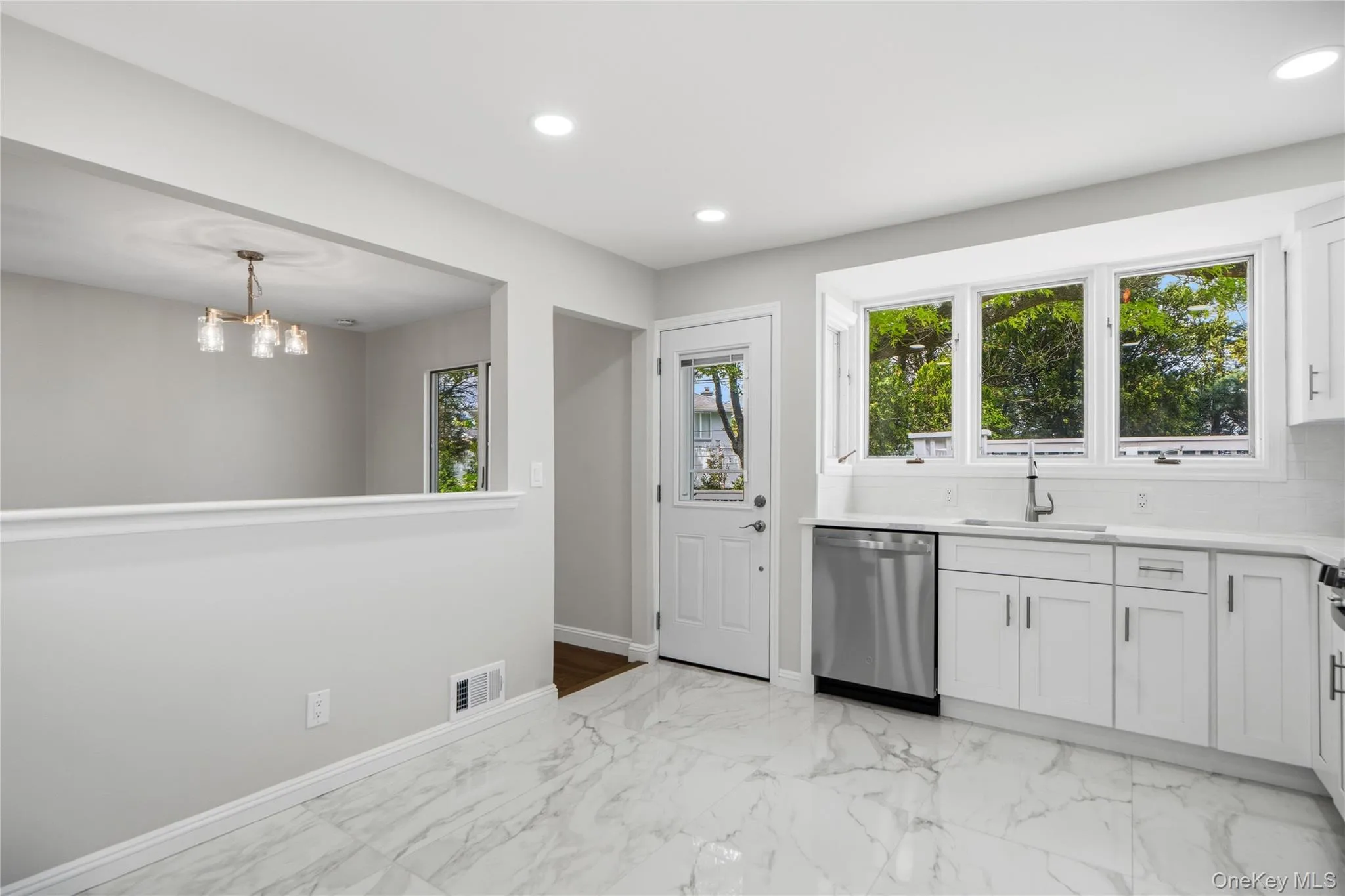Kitchen featuring white cabinetry, stainless steel dishwasher, a single basin sink, and white subway tile backsplash plus door to the Back Deck Kitchen featuring white cabinetry, stainless steel dishwasher, a single basin sink, and white subway tile backsplash plus door to the Back Deck