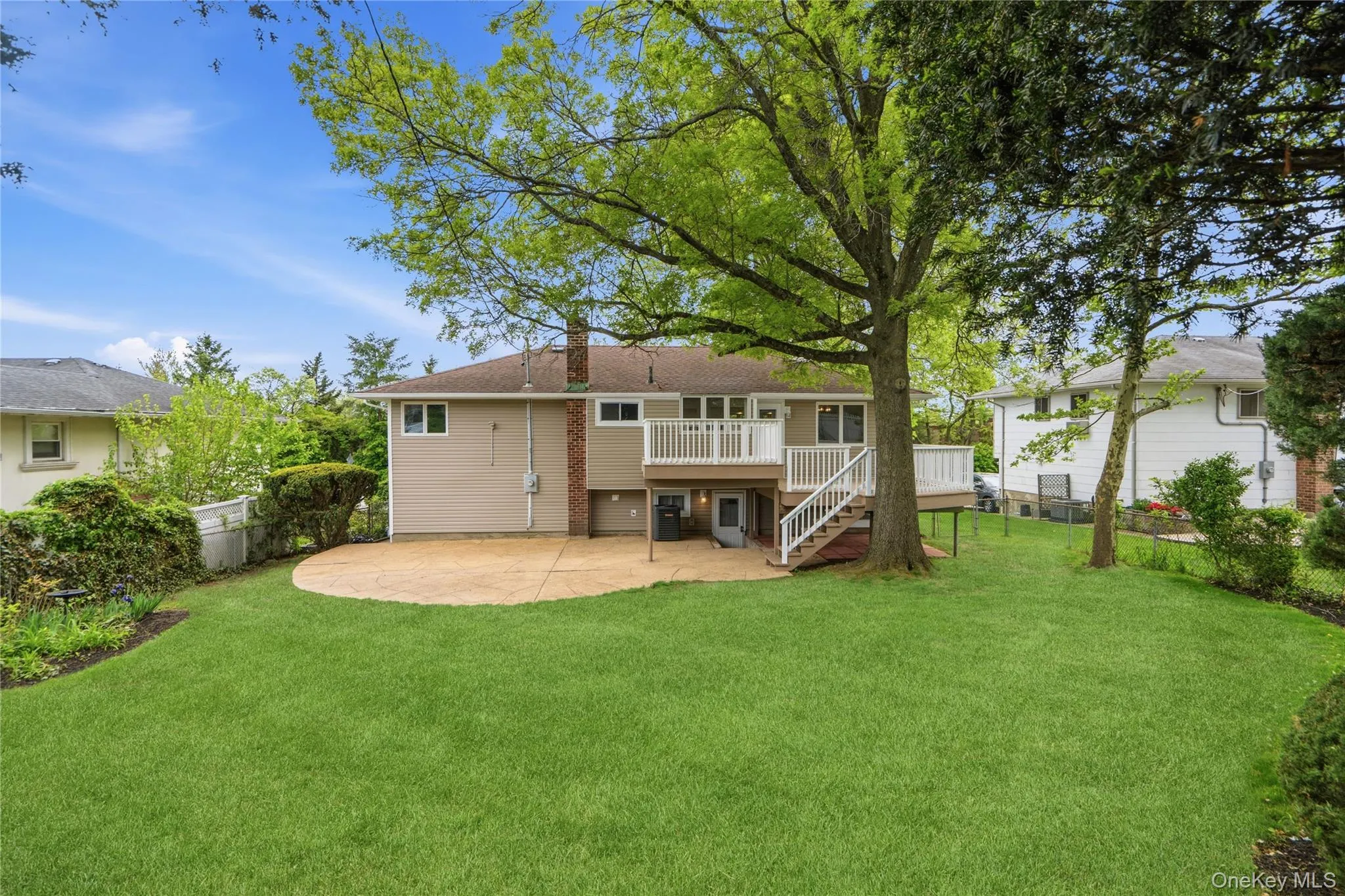 Expansive green lawn with mature trees, a concrete patio, a multi-level wood deck, and an exterior with siding and brick accents Expansive green lawn with mature trees, a concrete patio, a multi-level wood deck, and an exterior with siding and brick accents