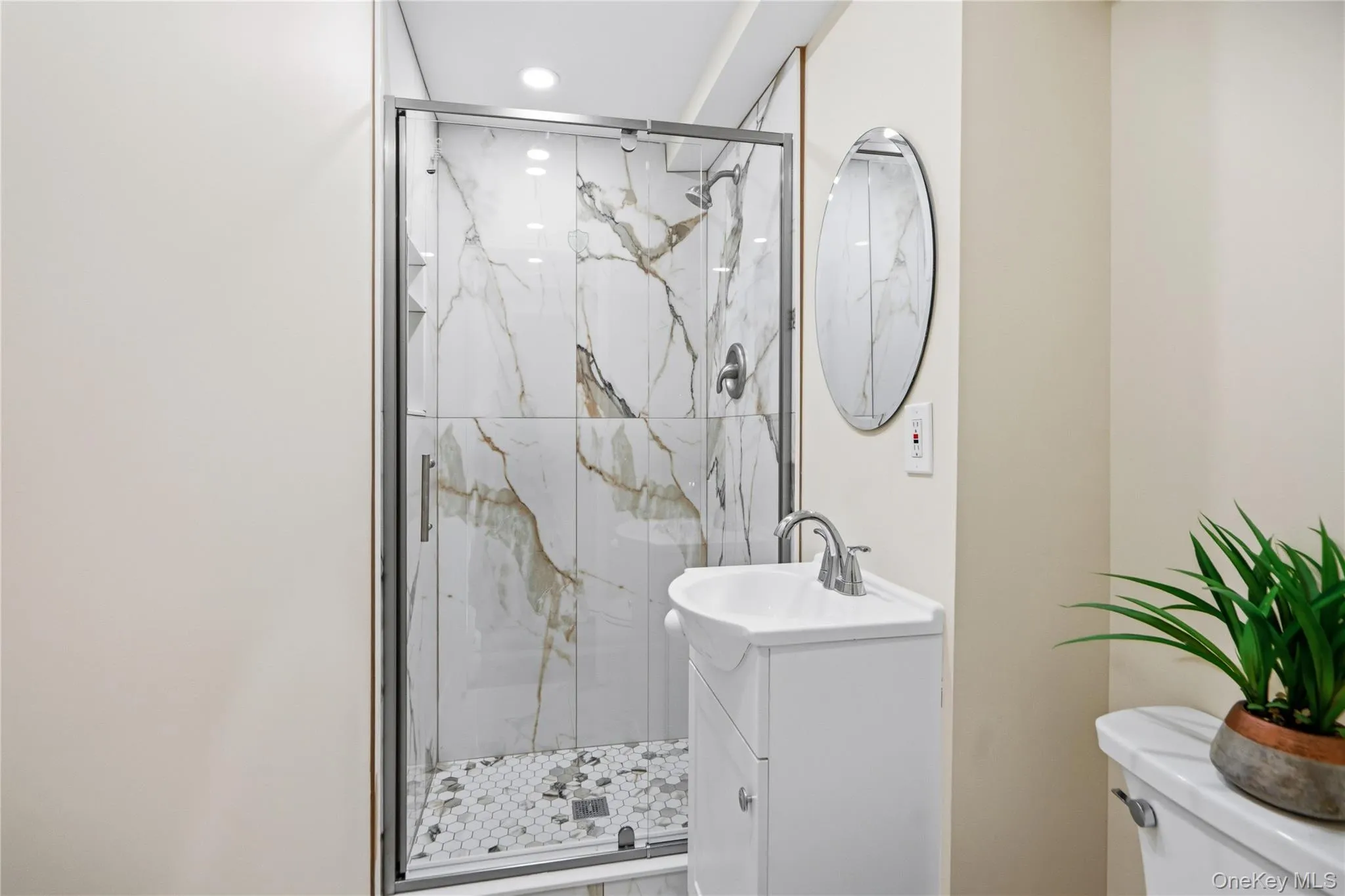 Shower enclosure with glass door, large format tile surround, and hexagonal tile floor Shower enclosure with glass door, large format tile surround, and hexagonal tile floor