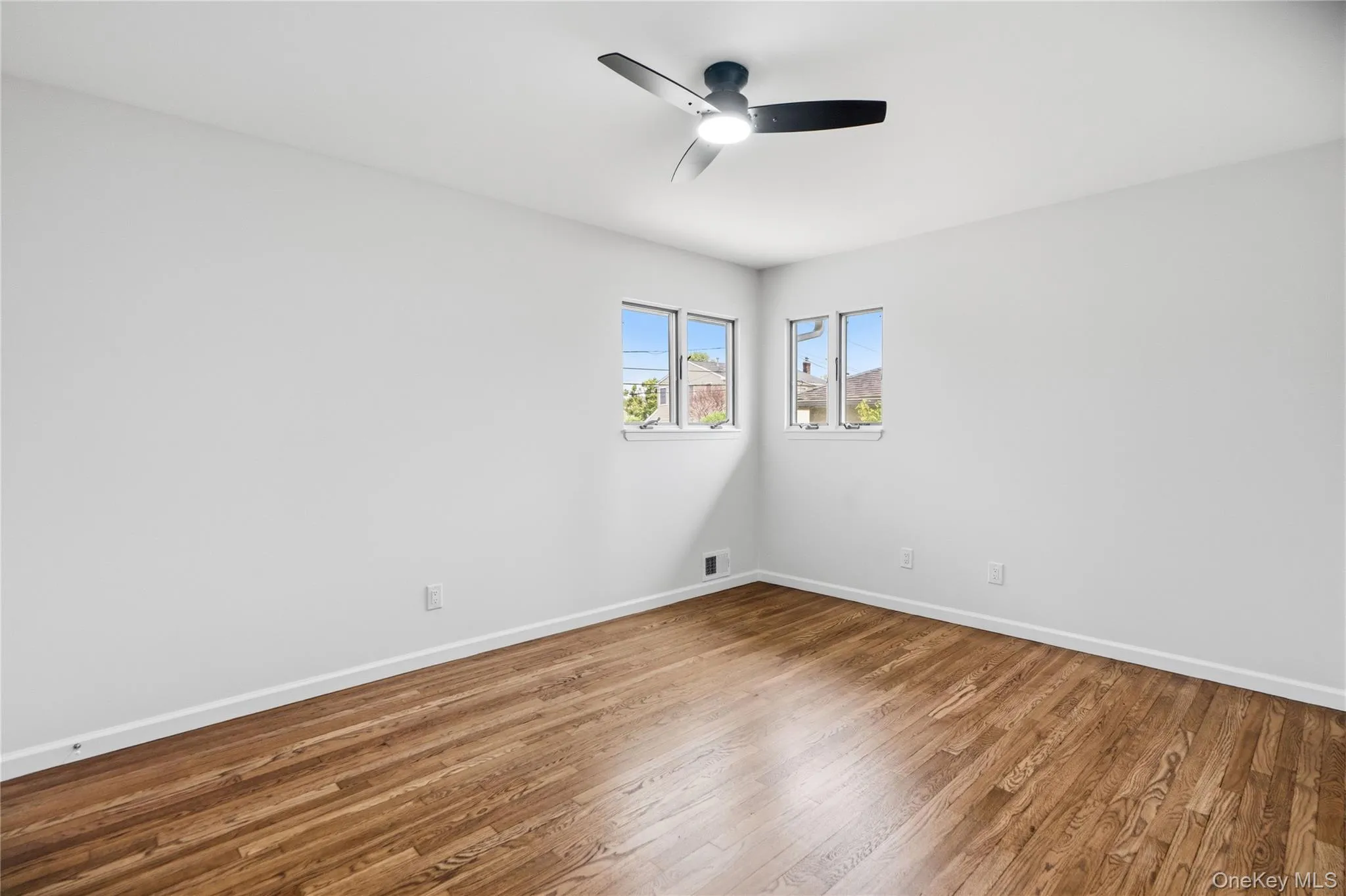 Bright interior room featuring wood-finish flooring, white baseboards, and white walls Bright interior room featuring wood-finish flooring, white baseboards, and white walls