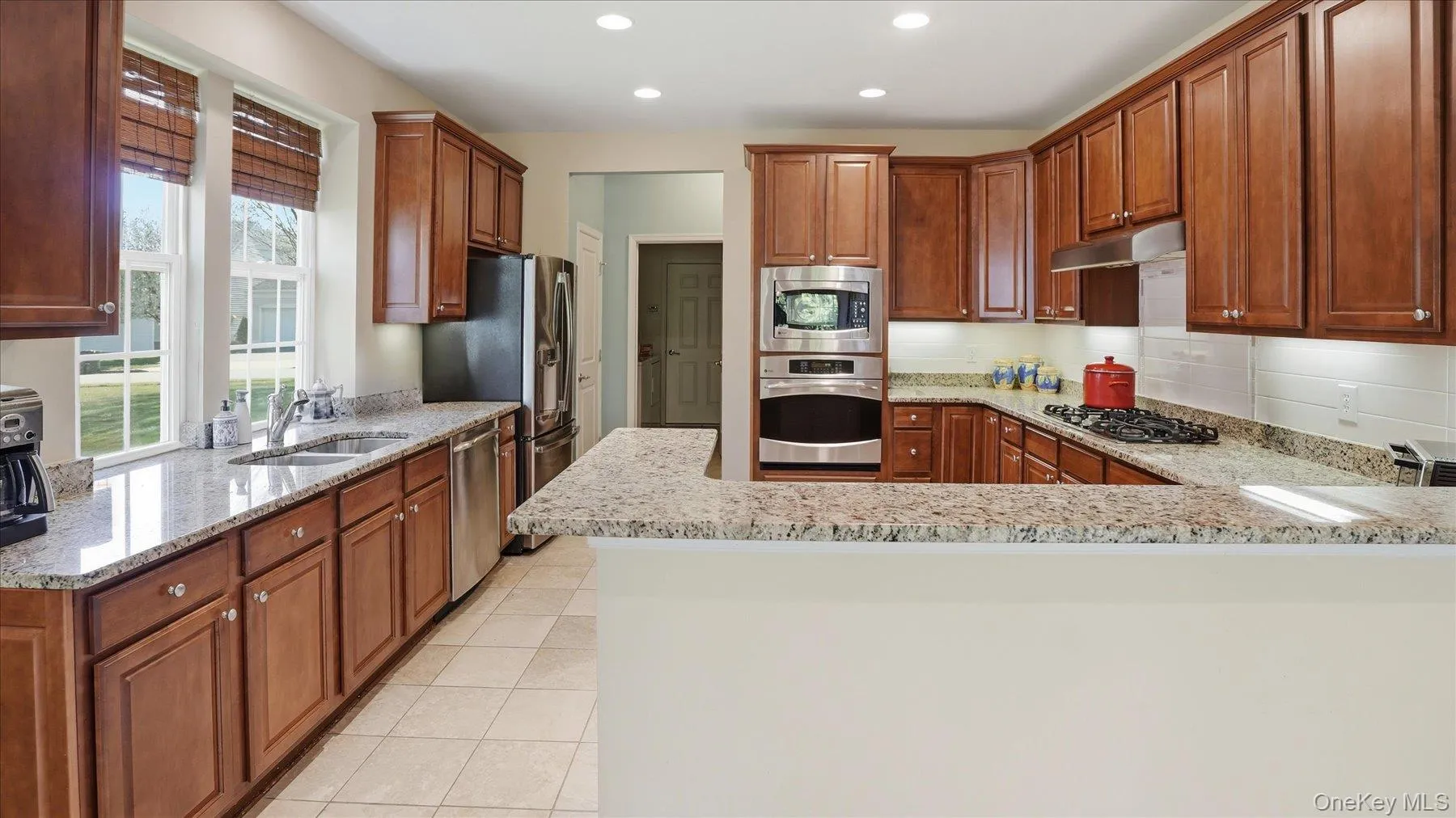 U-shaped kitchen featuring wood cabinetry, granite countertops, stainless steel appliances, and a tiled backsplash U-shaped kitchen featuring wood cabinetry, granite countertops, stainless steel appliances, and a tiled backsplash