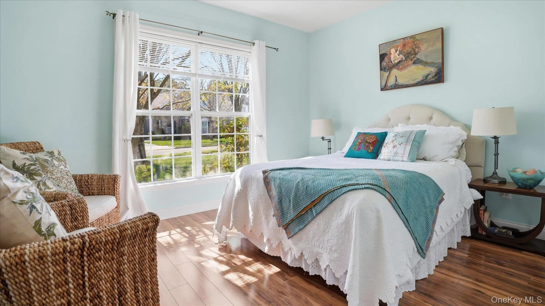 Bright room featuring a large window with muntins, light blue walls, and wood-finish flooring Bright room featuring a large window with muntins, light blue walls, and wood-finish flooring