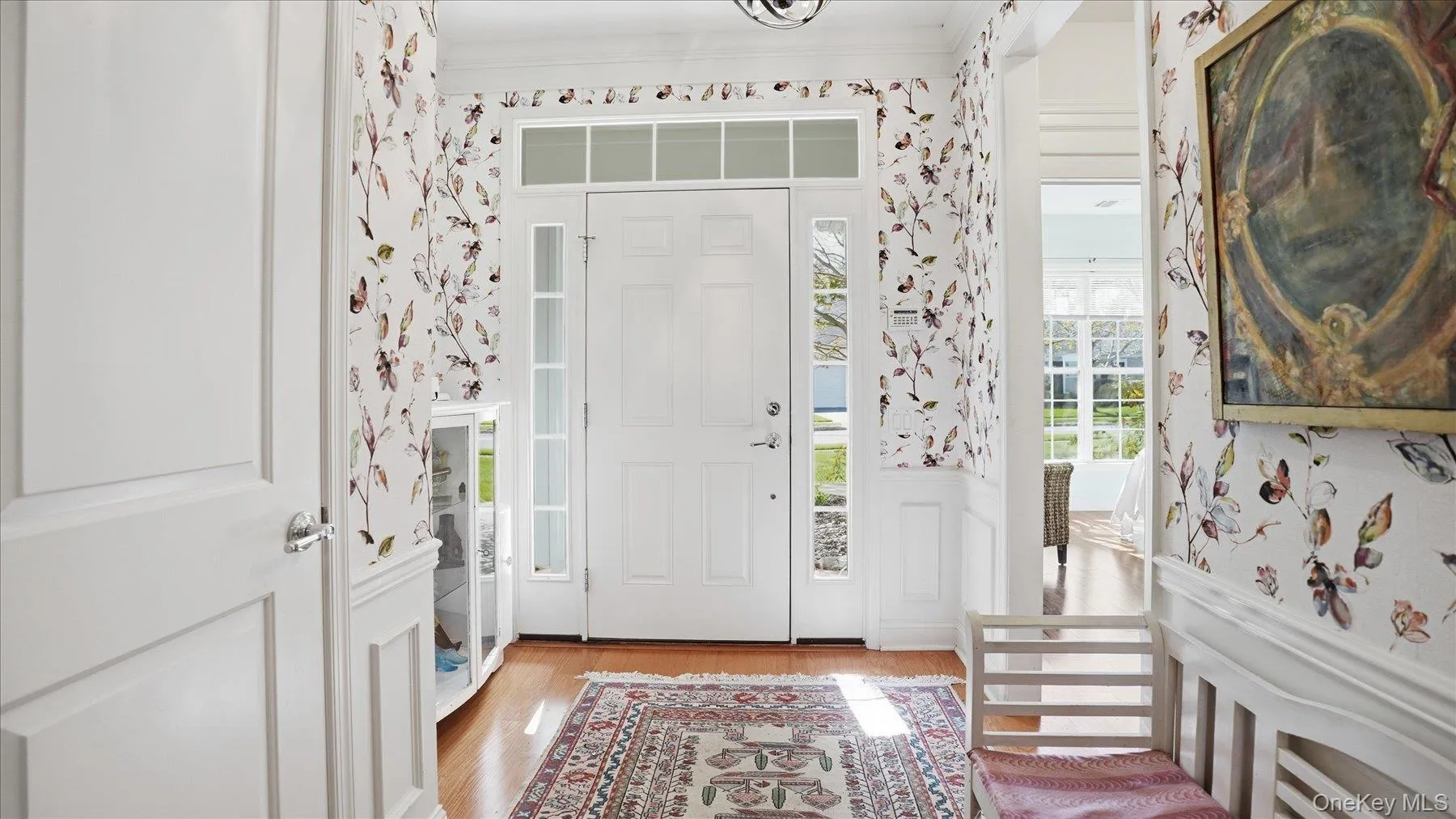 Inviting entry hall featuring wood-finish flooring, wainscoting, and patterned wallpaper Inviting entry hall featuring wood-finish flooring, wainscoting, and patterned wallpaper