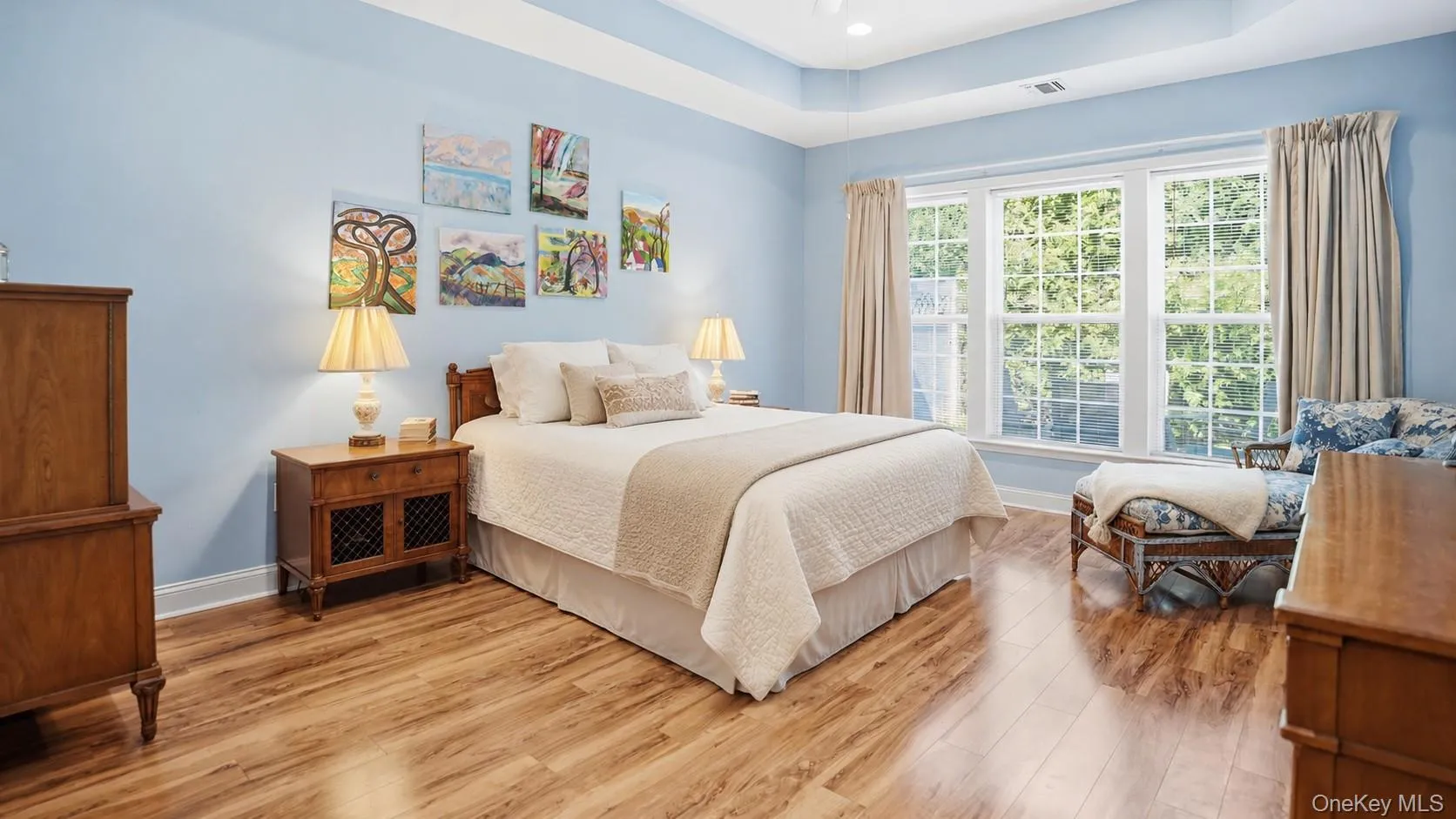 Tray ceiling bedroom featuring wood-finish flooring and a large triple window with white trim Tray ceiling bedroom featuring wood-finish flooring and a large triple window with white trim