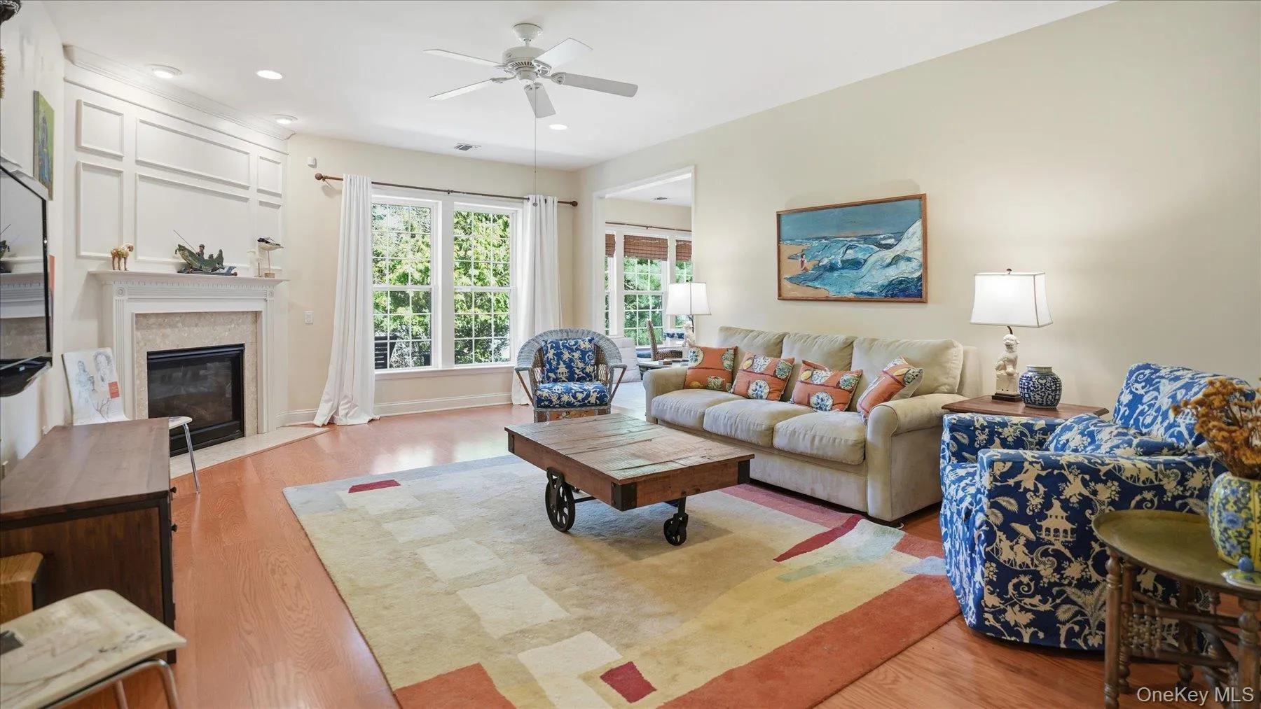 Living area featuring wood-finish flooring, a fireplace with a stone surround and white mantel, and a multi-pane window Living area featuring wood-finish flooring, a fireplace with a stone surround and white mantel, and a multi-pane window