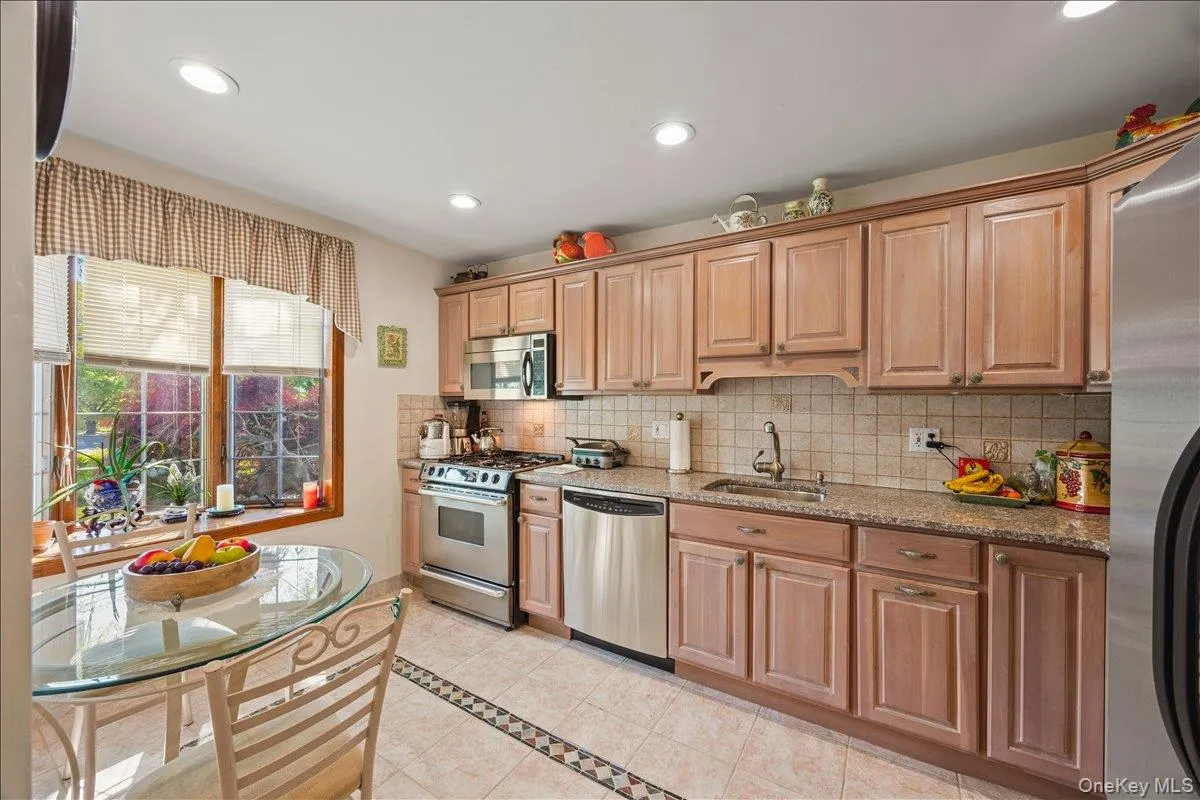 Kitchen featuring honey-toned wood cabinetry, stainless steel appliances, speckled countertops, and a ceramic tile backsplash Kitchen featuring honey-toned wood cabinetry, stainless steel appliances, speckled countertops, and a ceramic tile backsplash