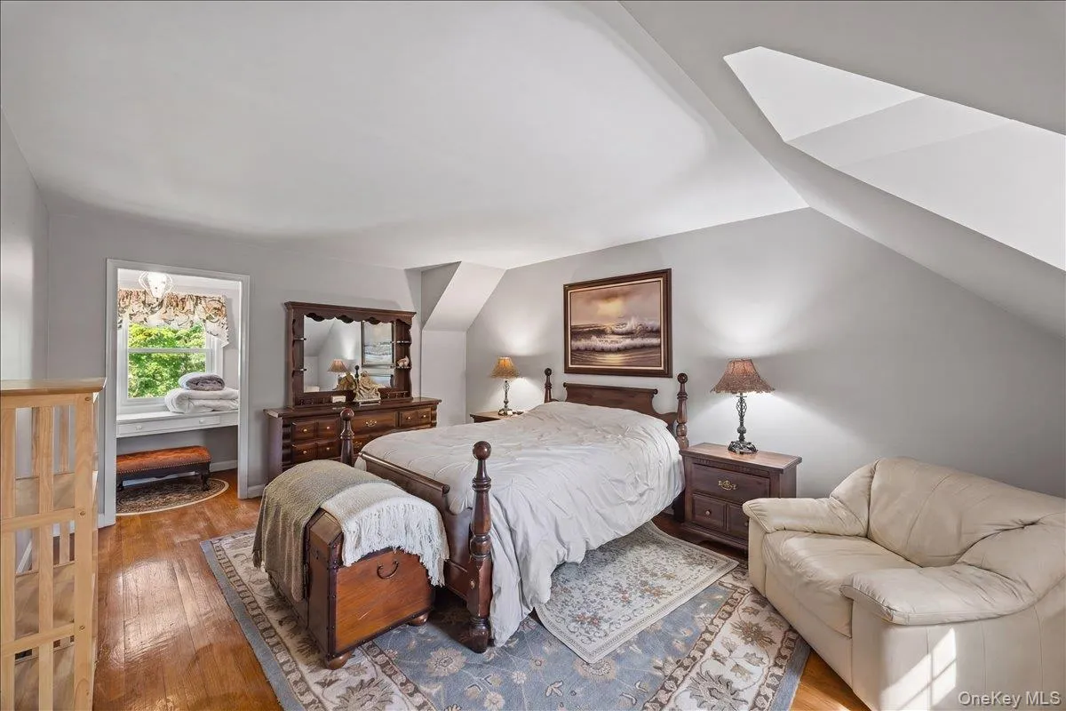 Sloped ceiling bedroom featuring warm wood-finish flooring, a recessed window area with a sill, and soft gray wall paint Sloped ceiling bedroom featuring warm wood-finish flooring, a recessed window area with a sill, and soft gray wall paint