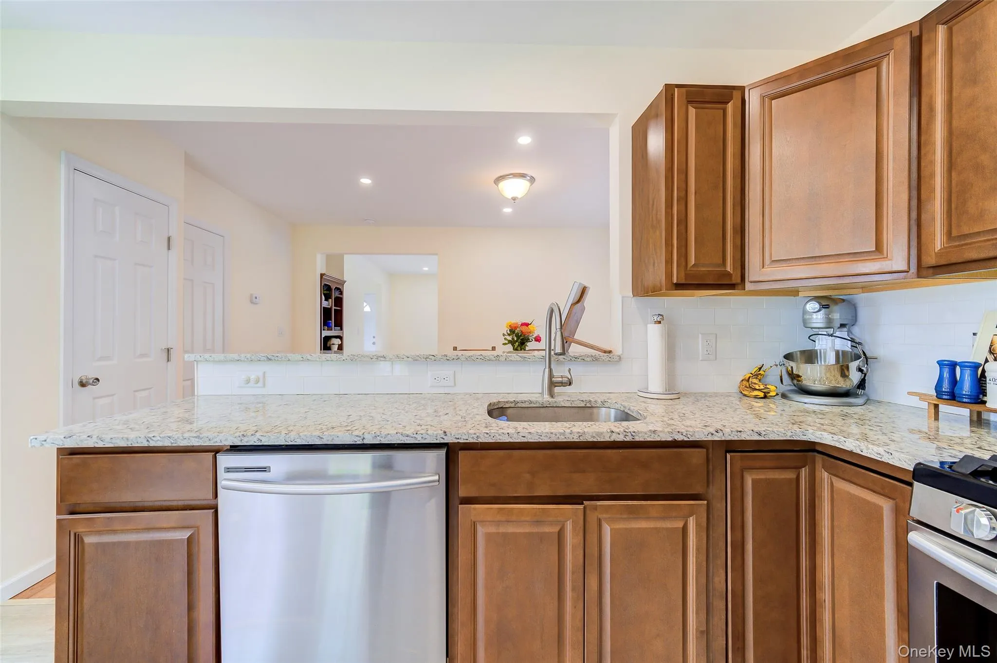 Kitchen featuring granite countertops, wood cabinetry, stainless steel dishwasher, undermount sink, and a white subway tile backsplash Kitchen featuring granite countertops, wood cabinetry, stainless steel dishwasher, undermount sink, and a white subway tile backsplash