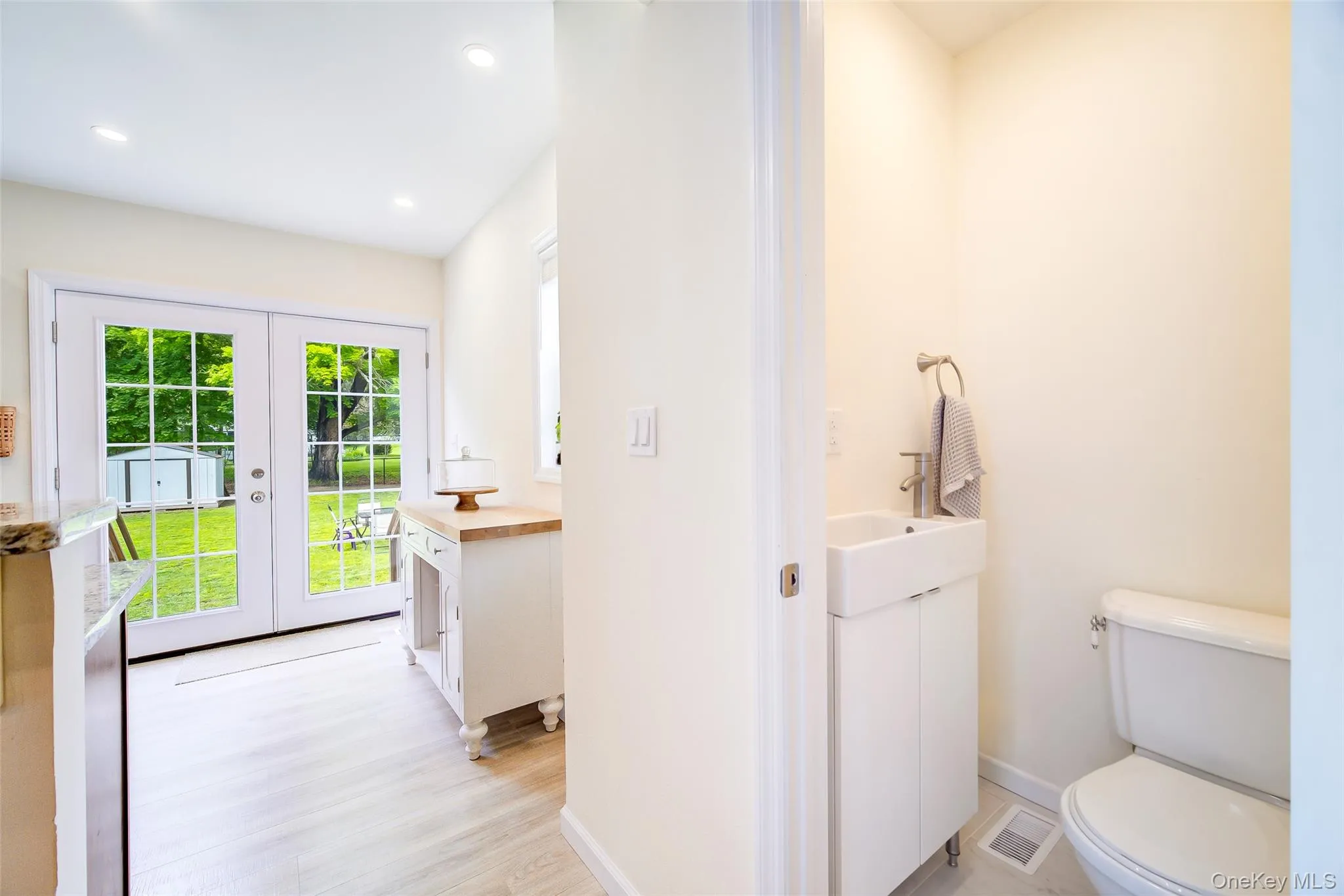 Double French doors with divided lites, recessed lighting, wood-finish flooring, white vanity with integrated sink, and a white toilet Double French doors with divided lites, recessed lighting, wood-finish flooring, white vanity with integrated sink, and a white toilet