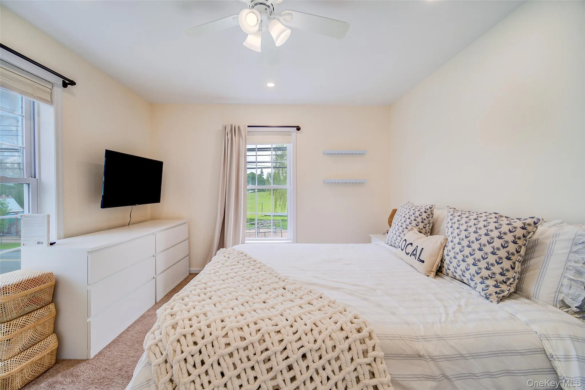 Master bedroom featuring a ceiling fan with integrated lighting, recessed lighting, two windows with window treatments, and wall-mounted shelving Master bedroom featuring a ceiling fan with integrated lighting, recessed lighting, two windows with window treatments, and wall-mounted shelving