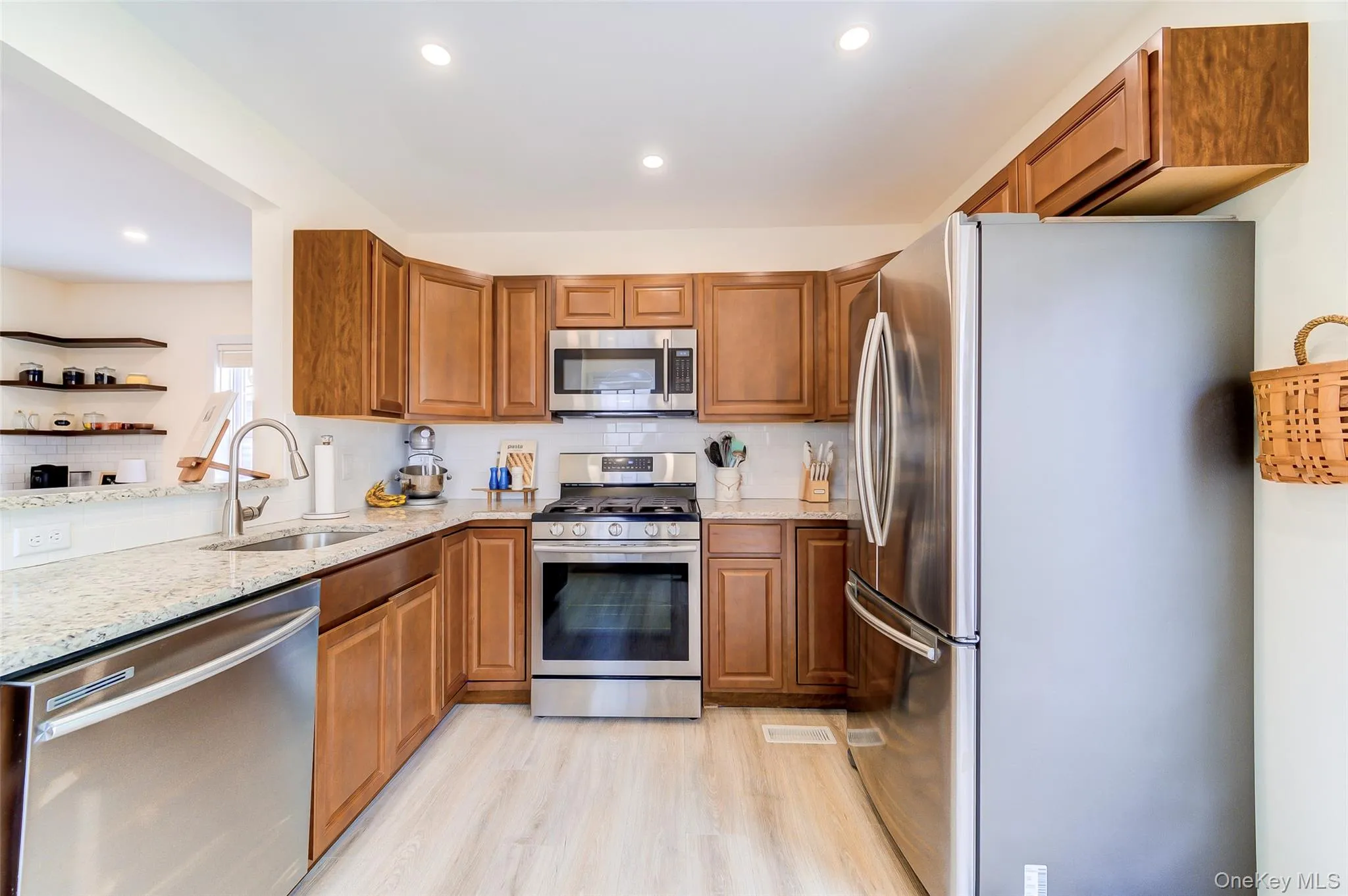 Kitchen featuring wood-finish cabinetry, stainless steel appliances, granite countertops, tile backsplash, and light wood-finish flooring Kitchen featuring wood-finish cabinetry, stainless steel appliances, granite countertops, tile backsplash, and light wood-finish flooring