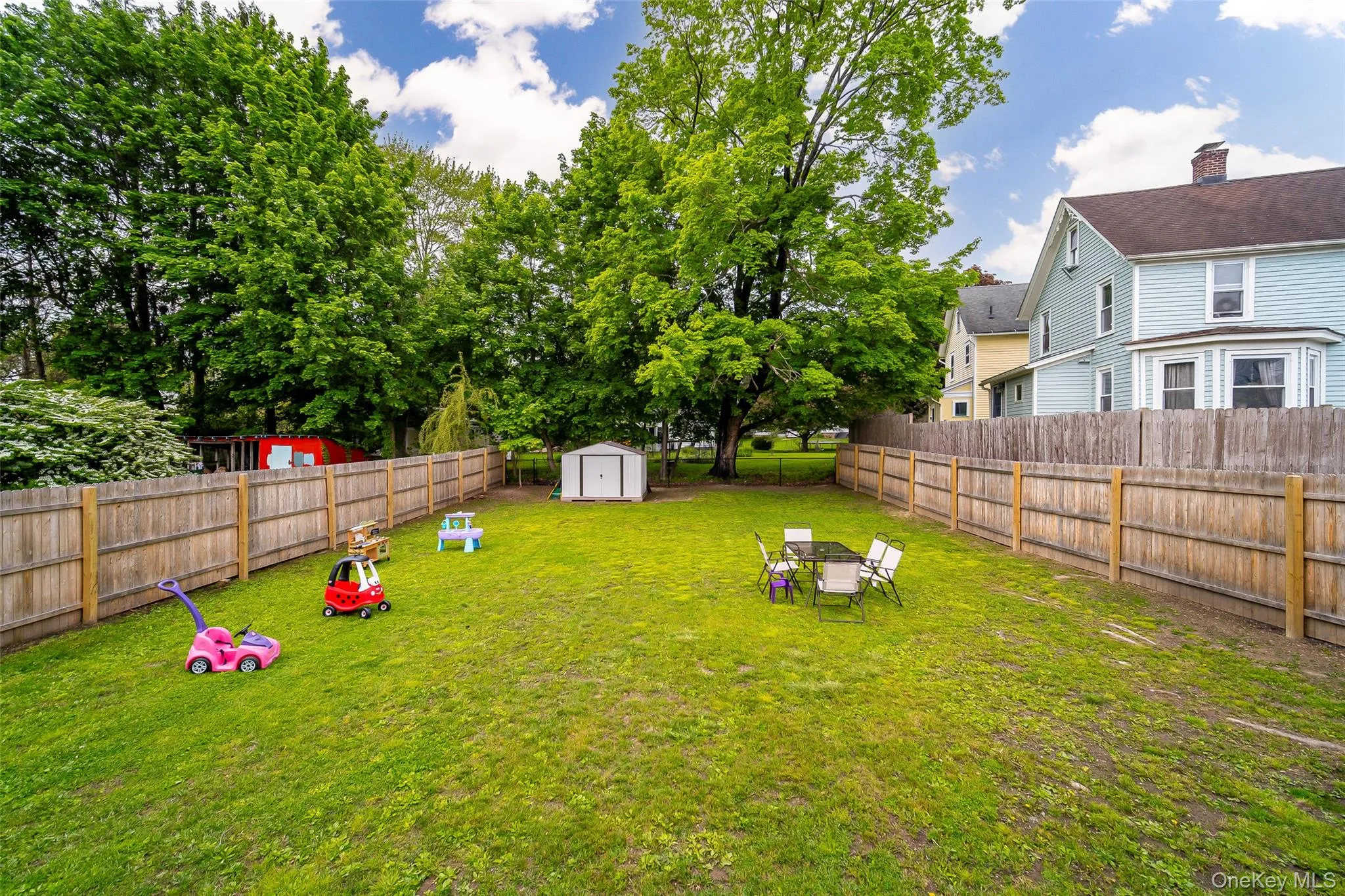 Spacious backyard featuring a full perimeter wood privacy fence, expansive green lawn, mature trees, and an outdoor storage shed Spacious backyard featuring a full perimeter wood privacy fence, expansive green lawn, mature trees, and an outdoor storage shed