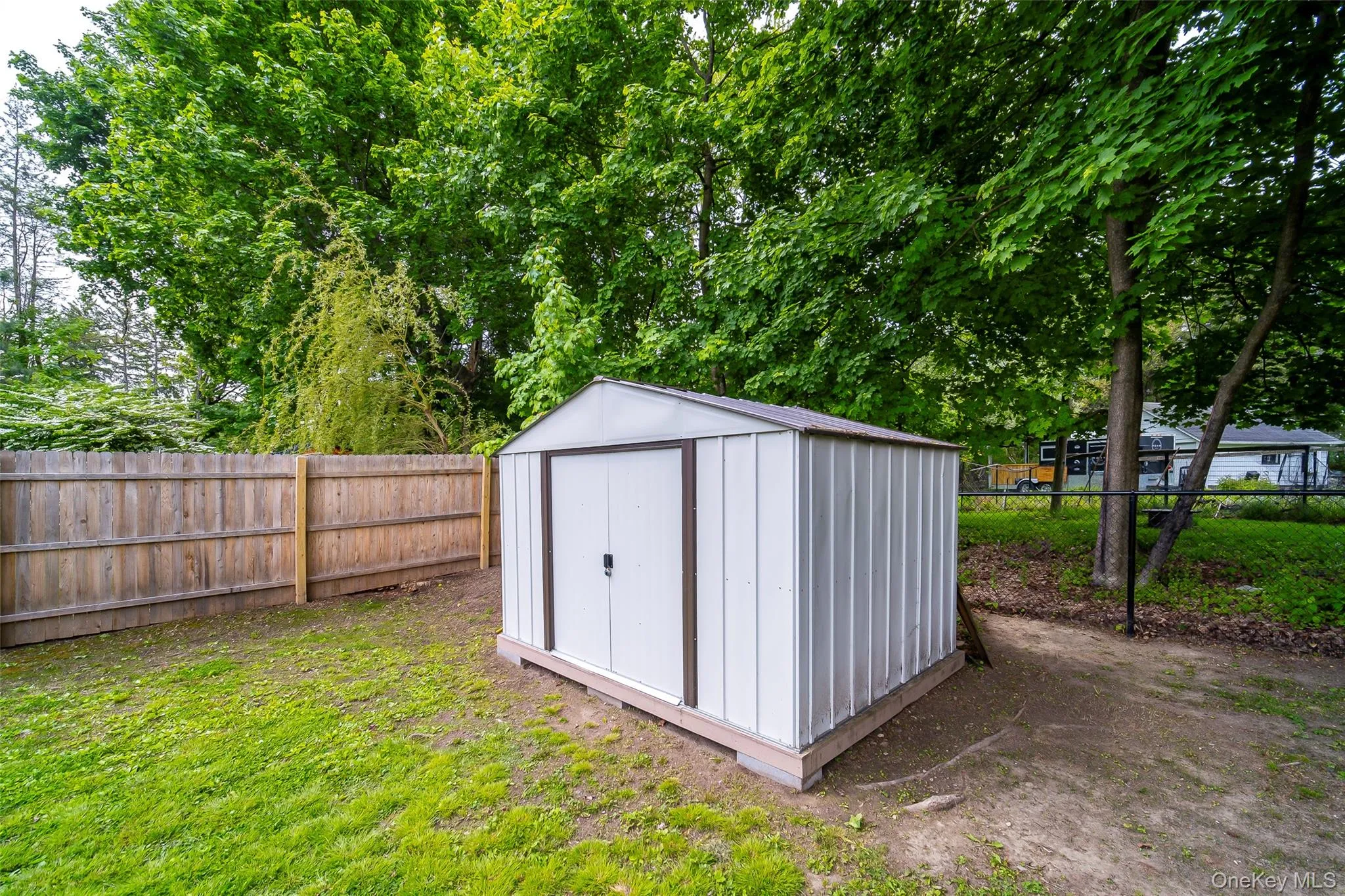 Freestanding storage shed with double doors, wood fencing, and mature trees Freestanding storage shed with double doors, wood fencing, and mature trees