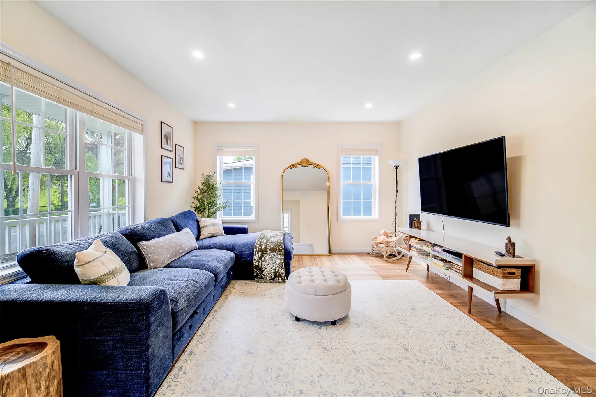 Spacious living area featuring expansive windows, recessed lighting, wood-finish flooring, a contemporary floating media console, and light-toned walls Spacious living area featuring expansive windows, recessed lighting, wood-finish flooring, a contemporary floating media console, and light-toned walls