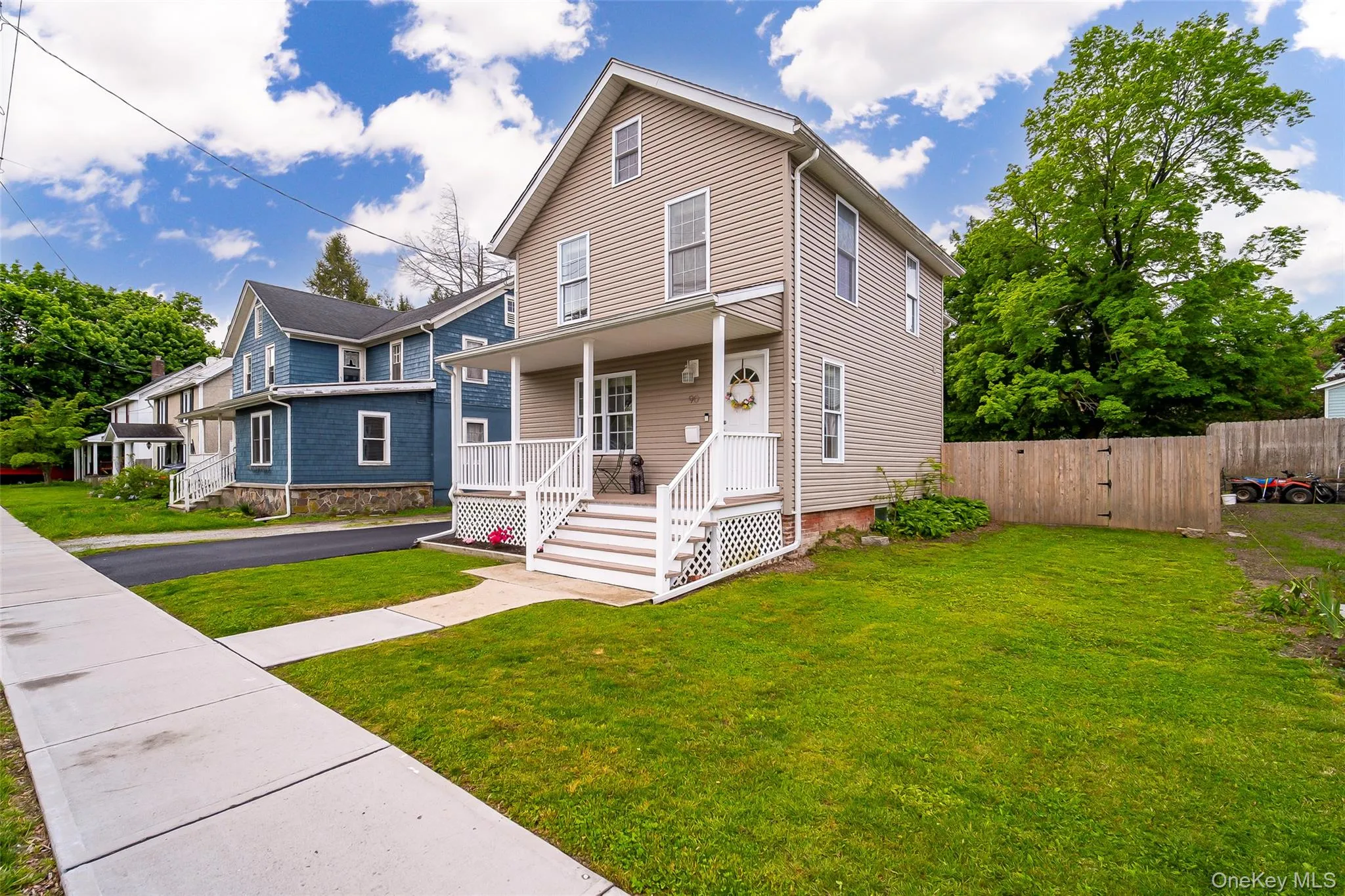 Two-story residence featuring light-colored siding, a covered front porch with white railings, and a front yard with established green space Two-story residence featuring light-colored siding, a covered front porch with white railings, and a front yard with established green space