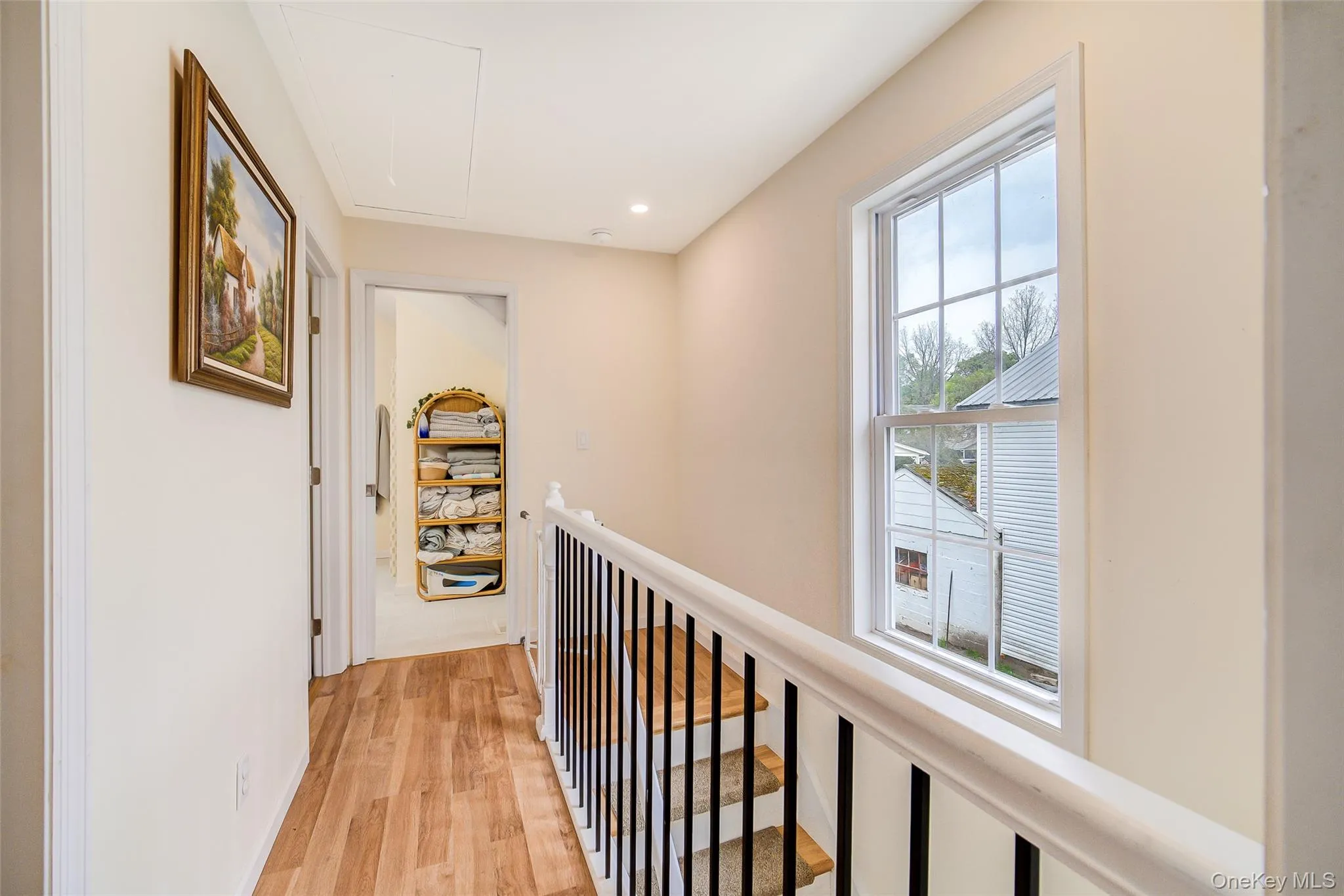 Well-lit hallway featuring wood-finish flooring, a white spindle and handrail staircase, and a large window with muntins Well-lit hallway featuring wood-finish flooring, a white spindle and handrail staircase, and a large window with muntins