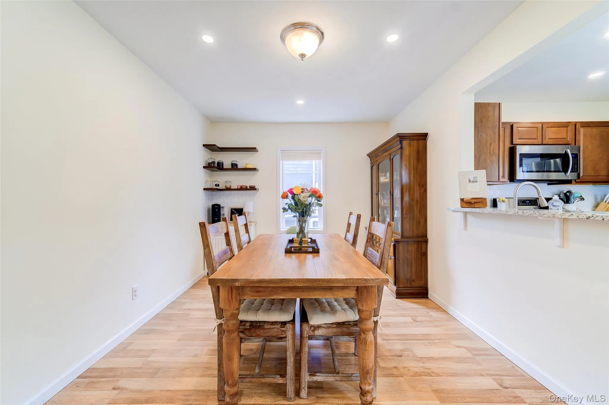 Open-concept dining area with wood-finish flooring, recessed lighting, and a pass-through opening to the kitchen Open-concept dining area with wood-finish flooring, recessed lighting, and a pass-through opening to the kitchen