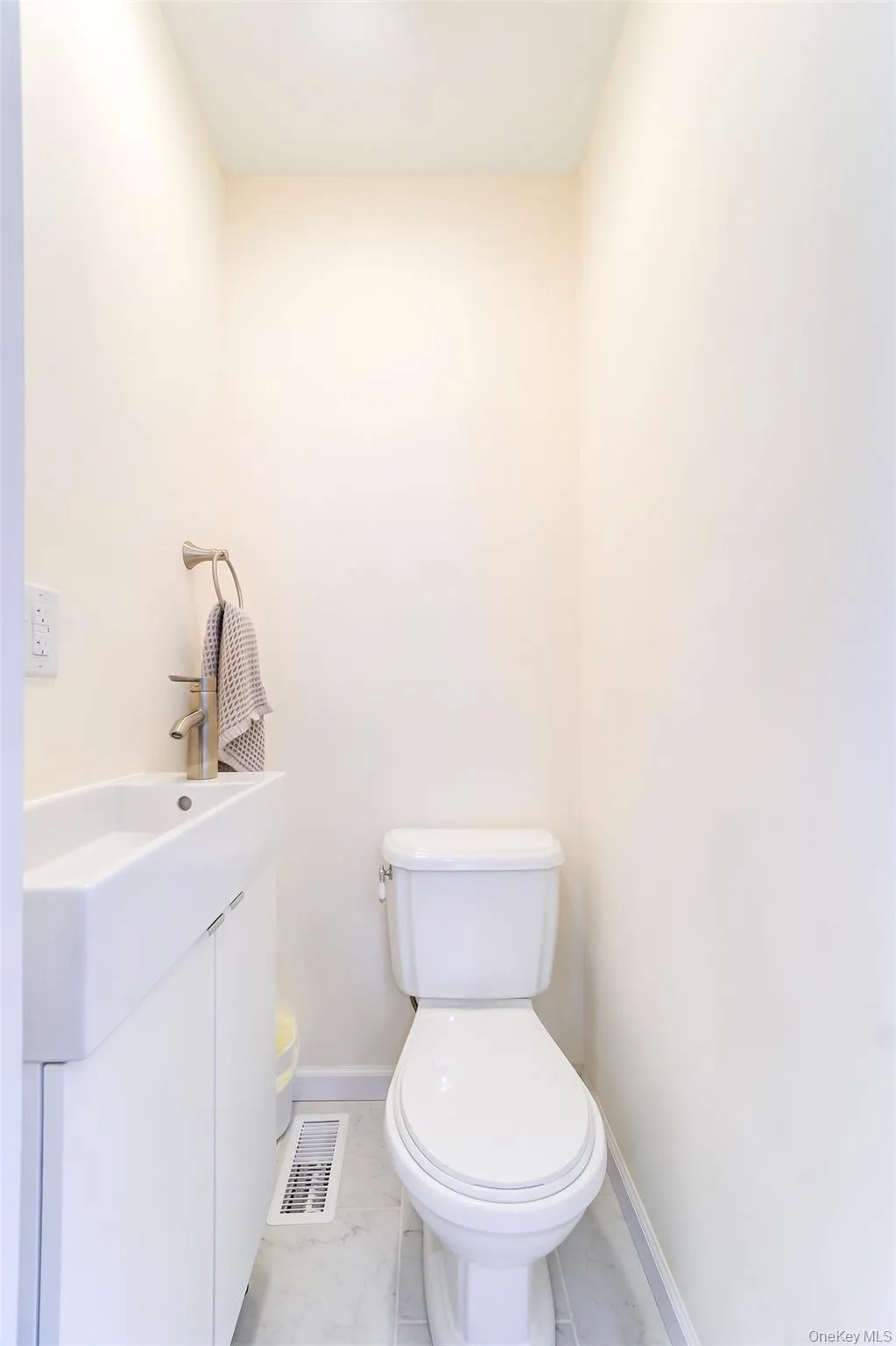 Well-lit powder room featuring a white toilet, a modern vanity with integrated sink, a sleek faucet, and light-toned tile flooring Well-lit powder room featuring a white toilet, a modern vanity with integrated sink, a sleek faucet, and light-toned tile flooring