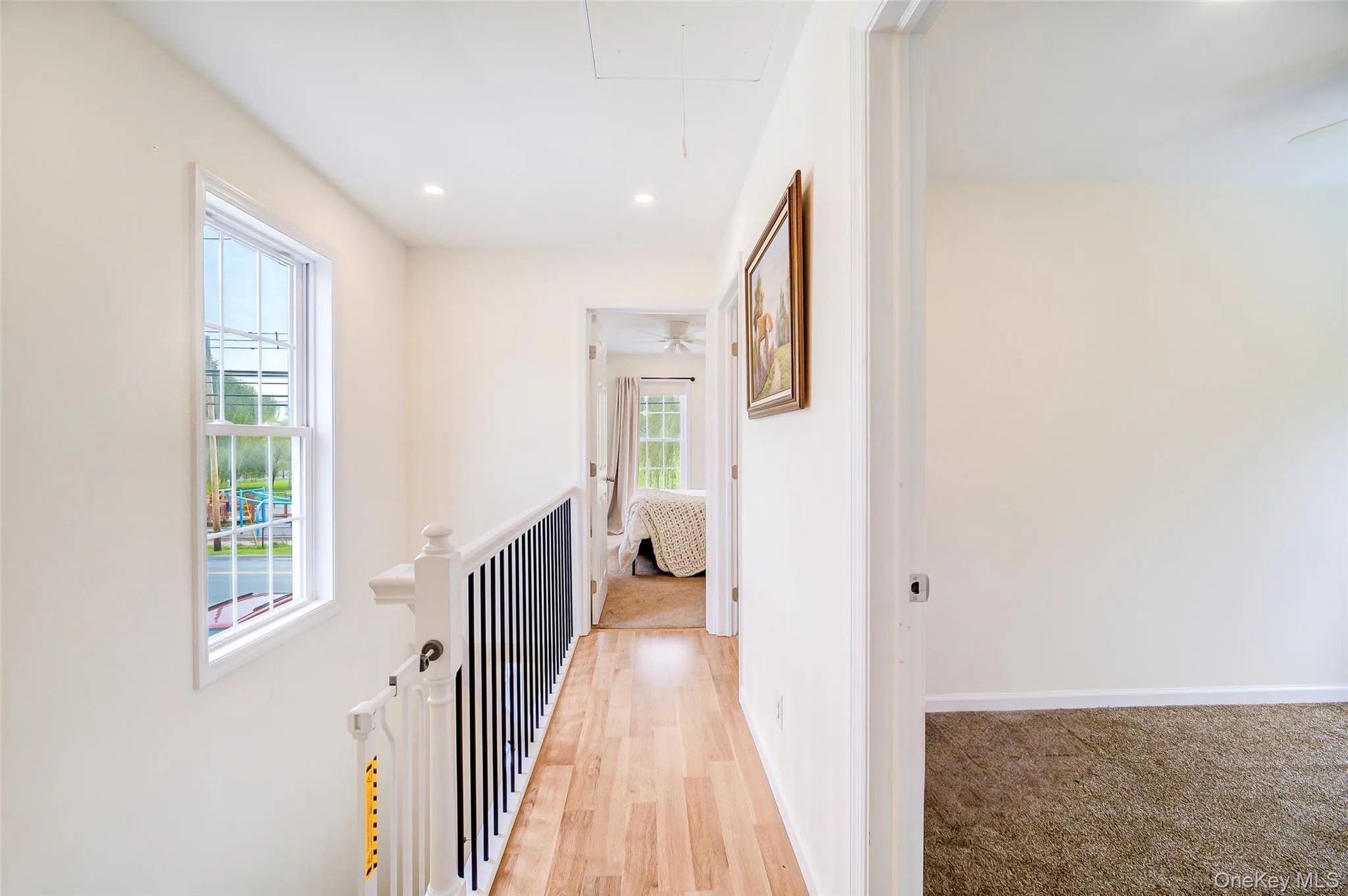 Upper-level hallway featuring wood-finish flooring, recessed lighting, a white spindle staircase railing with black balusters, and a window providing natural light Upper-level hallway featuring wood-finish flooring, recessed lighting, a white spindle staircase railing with black balusters, and a window providing natural light