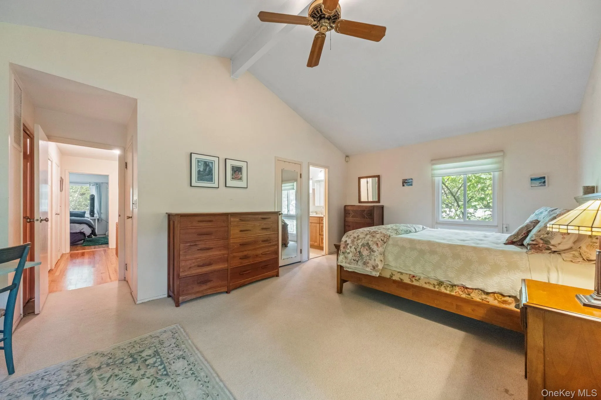 Carpeted bedroom with a vaulted ceiling, wood-finish ceiling fan, and a large window Carpeted bedroom with a vaulted ceiling, wood-finish ceiling fan, and a large window