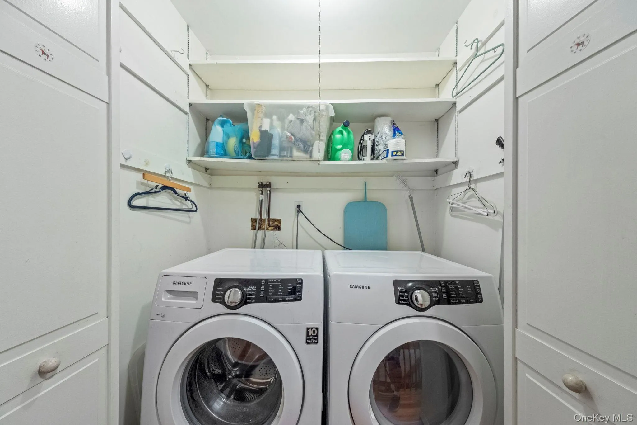Dedicated laundry area featuring a front-loading washer and dryer set, built-in shelving, and white cabinetry Dedicated laundry area featuring a front-loading washer and dryer set, built-in shelving, and white cabinetry