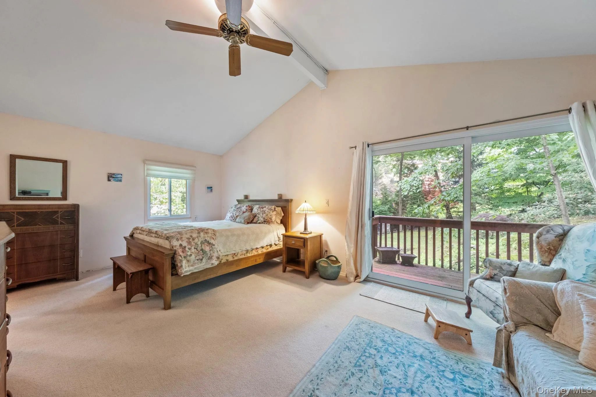 Vaulted ceiling bedroom with a ceiling fan, plush carpet flooring, a window, and sliding glass doors opening to a wood deck Vaulted ceiling bedroom with a ceiling fan, plush carpet flooring, a window, and sliding glass doors opening to a wood deck
