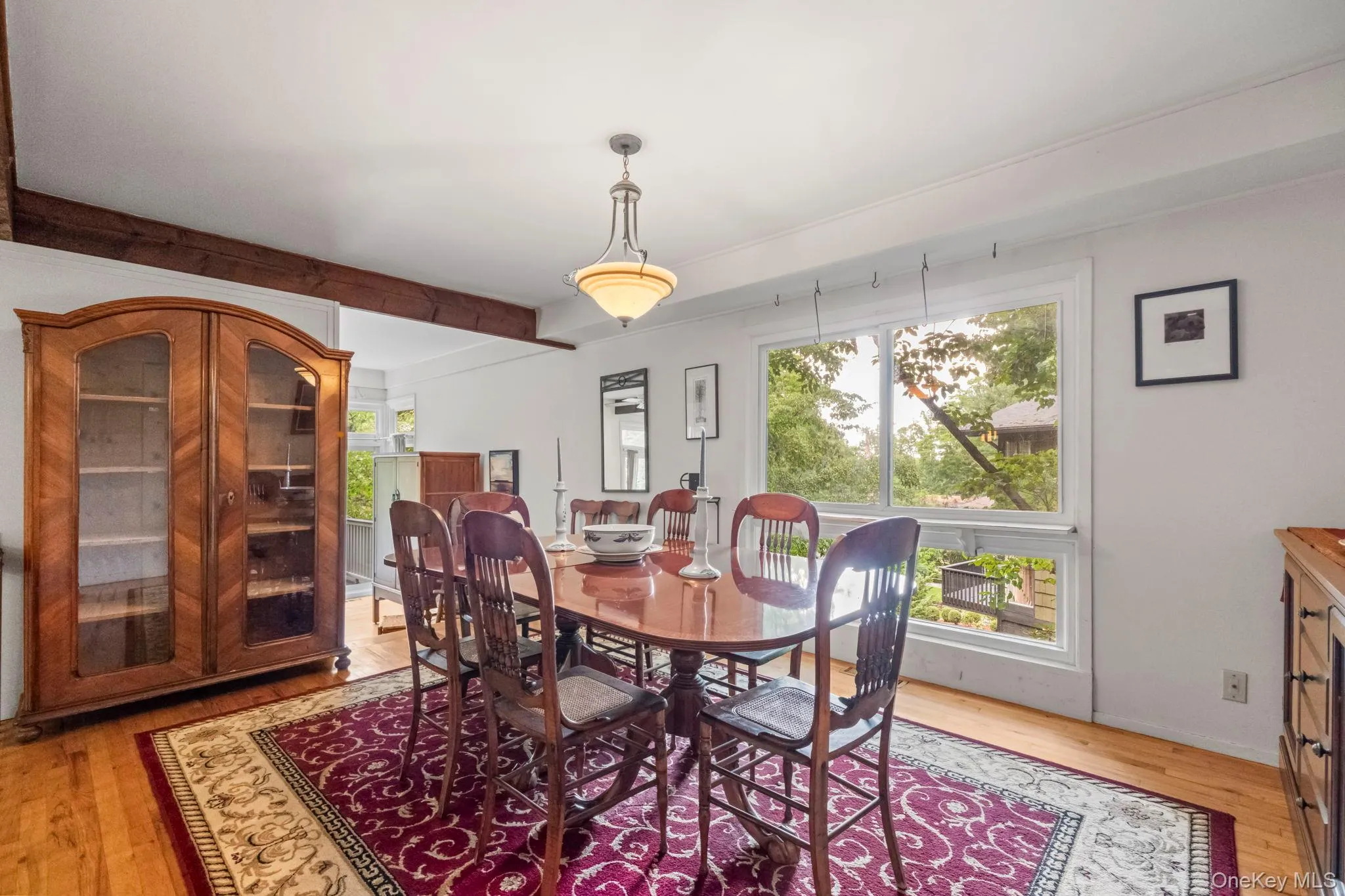 Bright dining area featuring hardwood flooring, exposed wood beam, large window, and an overhead chandelier fixture Bright dining area featuring hardwood flooring, exposed wood beam, large window, and an overhead chandelier fixture