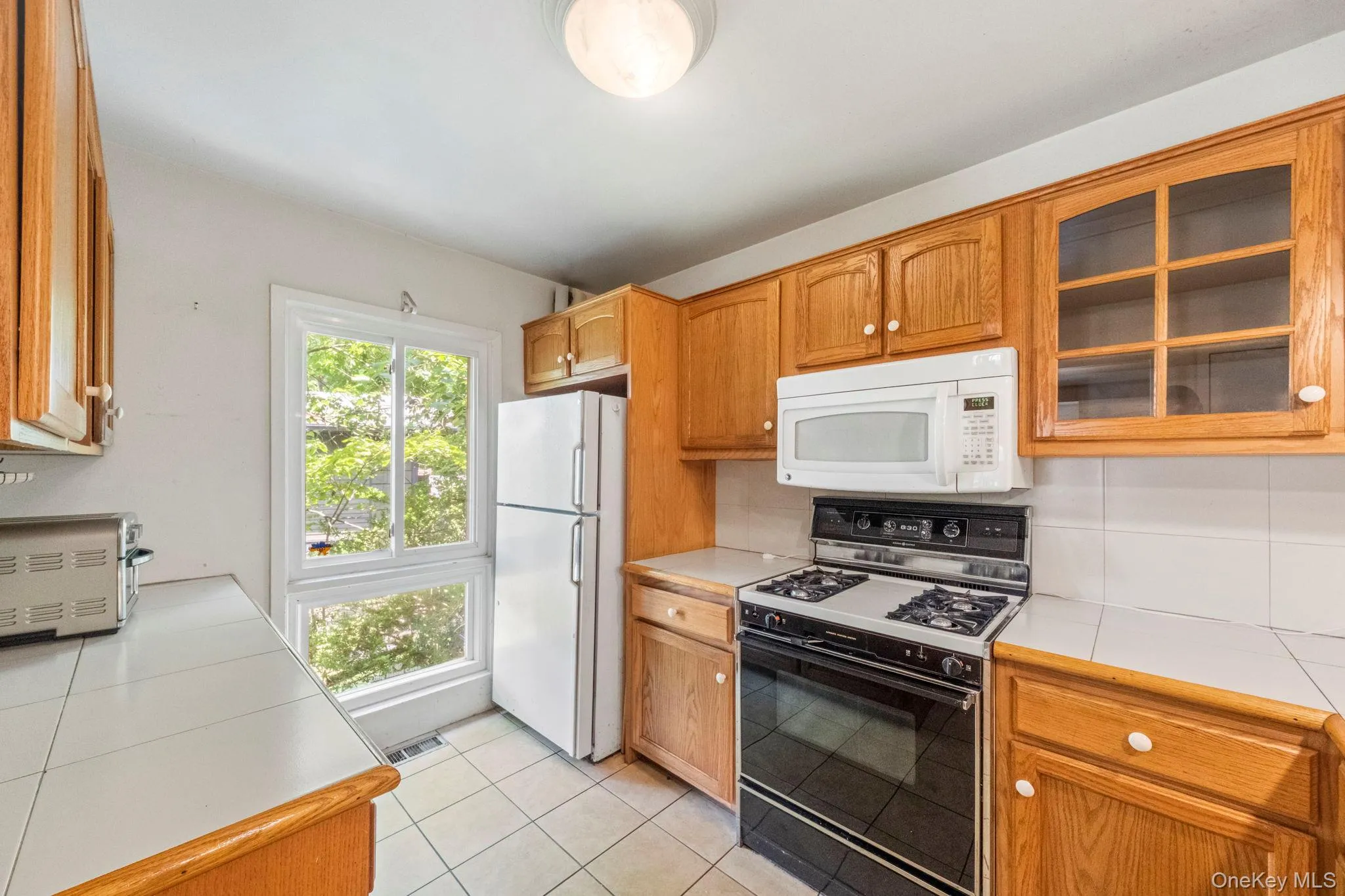 Kitchen featuring wood cabinetry, white tile countertops, and a white tile backsplash Kitchen featuring wood cabinetry, white tile countertops, and a white tile backsplash