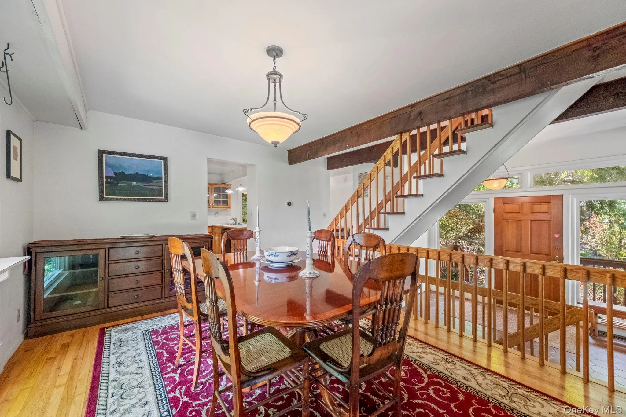 Dining area featuring hardwood flooring, exposed beam ceiling, a chandelier light fixture, and a wood staircase with wood balusters Dining area featuring hardwood flooring, exposed beam ceiling, a chandelier light fixture, and a wood staircase with wood balusters