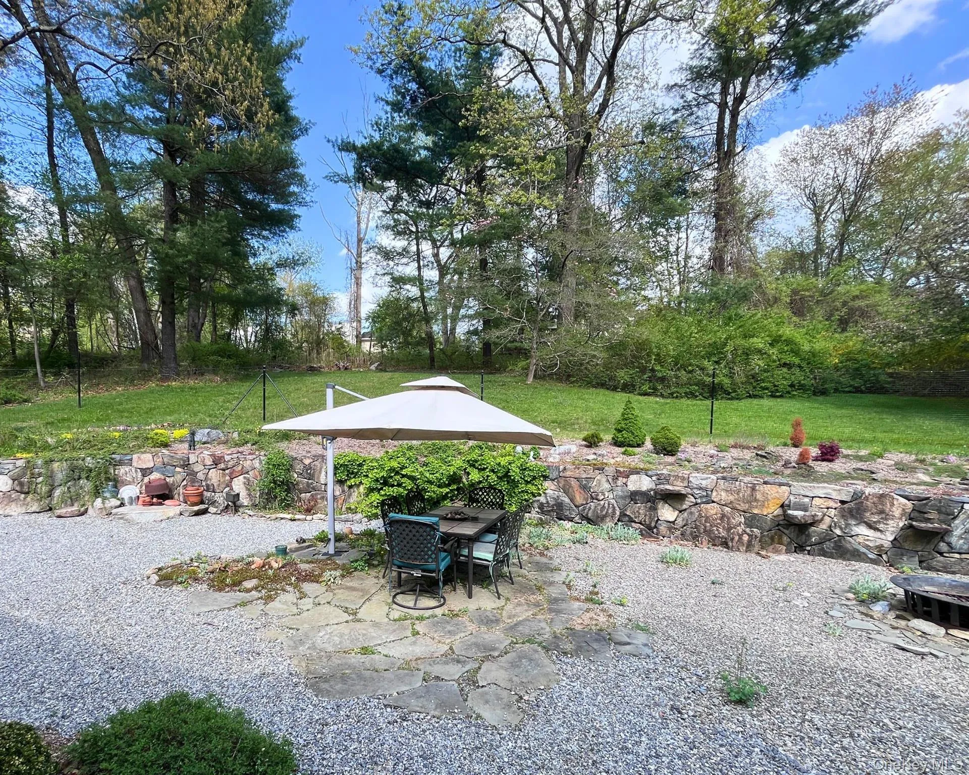 Patio with table, umbrella, and fire pit surrounded by lush landscaping Patio with table, umbrella, and fire pit surrounded by lush landscaping