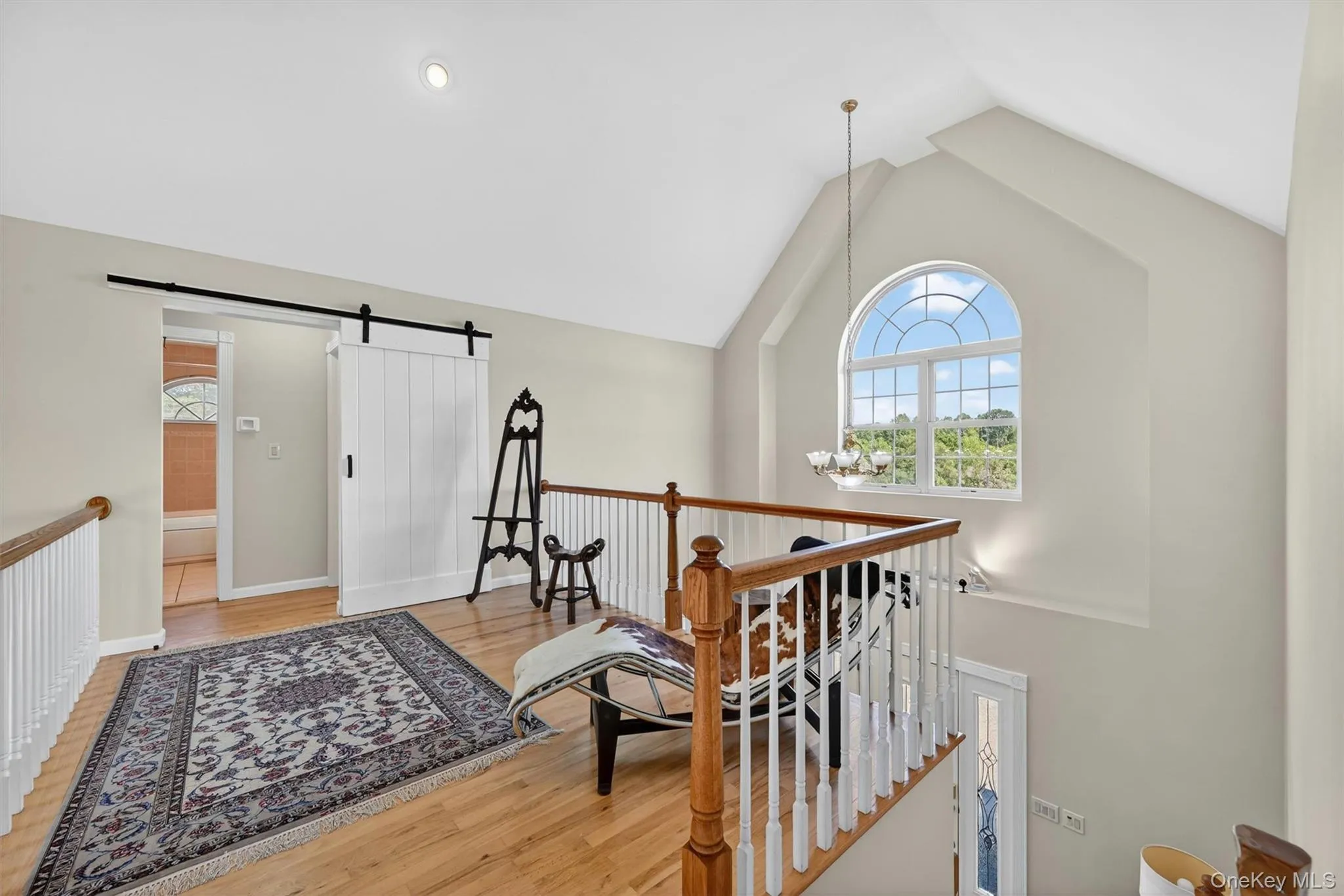 The upstairs landing offers a quiet, airy moment in the home, with vaulted ceilings, hardwood floors, and a beautiful arched window overlooking the main level. The upstairs landing offers a quiet, airy moment in the home, with vaulted ceilings, hardwood floors, and a beautiful arched window overlooking the main level.