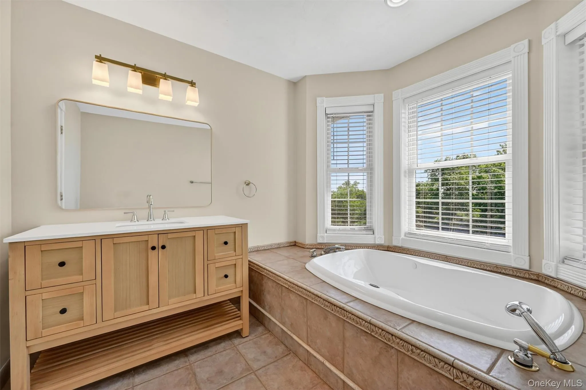 This bathroom offers a relaxing retreat with a soaking tub, updated vanity, large mirror, and natural light from the surrounding windows. Located adjacent to the first-floor bedroom, this full bath creates a comfortable main-level ensuite option. Use it as your primary suite, or, if you prefer the second-floor primary, this space becomes a private and welcoming guest suite for family or visitors. This bathroom offers a relaxing retreat with a soaking tub, updated vanity, large mirror, and natural light from the surrounding windows. Located adjacent to the first-floor bedroom, this full bath creates a comfortable main-level ensuite option. Use it as your primary suite, or, if you prefer the second-floor primary, this space becomes a private and welcoming guest suite for family or visitors.
