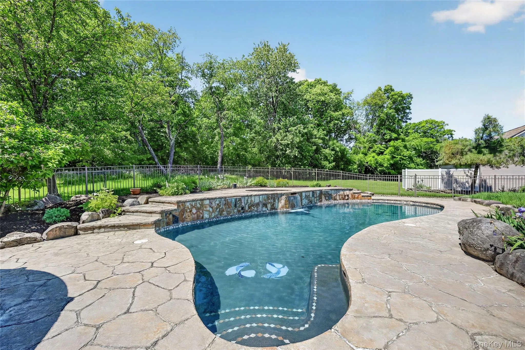 Surrounded by mature greenery and gentle water features, the pool area feels peaceful, private, and resort-like. The heated gunite pool is the centerpiece of this backyard retreat, complete with a raised hot tub and three beautiful waterfalls that cascade over the wall into the pool below. It is an inviting space designed for summer days, evening swims, and unforgettable gatherings at home. Surrounded by mature greenery and gentle water features, the pool area feels peaceful, private, and resort-like. The heated gunite pool is the centerpiece of this backyard retreat, complete with a raised hot tub and three beautiful waterfalls that cascade over the wall into the pool below. It is an inviting space designed for summer days, evening swims, and unforgettable gatherings at home.