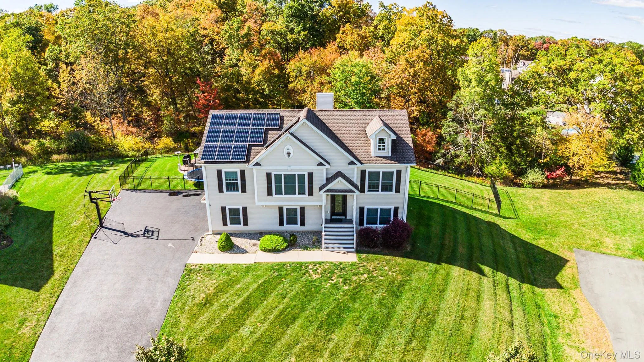 View of front facade featuring a chimney, solar panels, driveway, and a shingled roof View of front facade featuring a chimney, solar panels, driveway, and a shingled roof