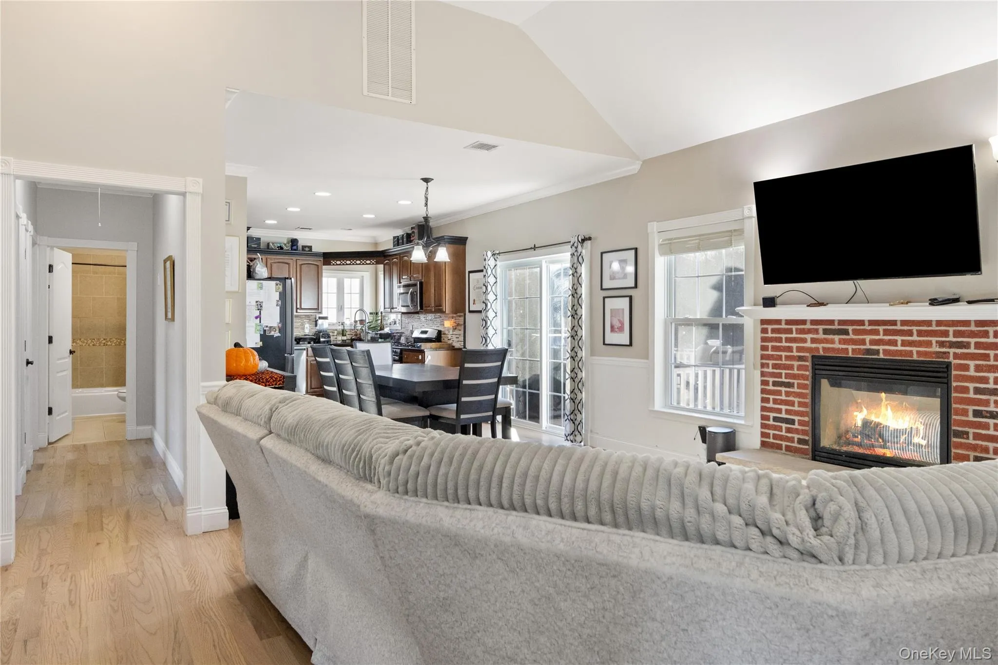 Living room with a fireplace, light wood-style flooring, lofted ceiling, crown molding, and recessed lighting Living room with a fireplace, light wood-style flooring, lofted ceiling, crown molding, and recessed lighting