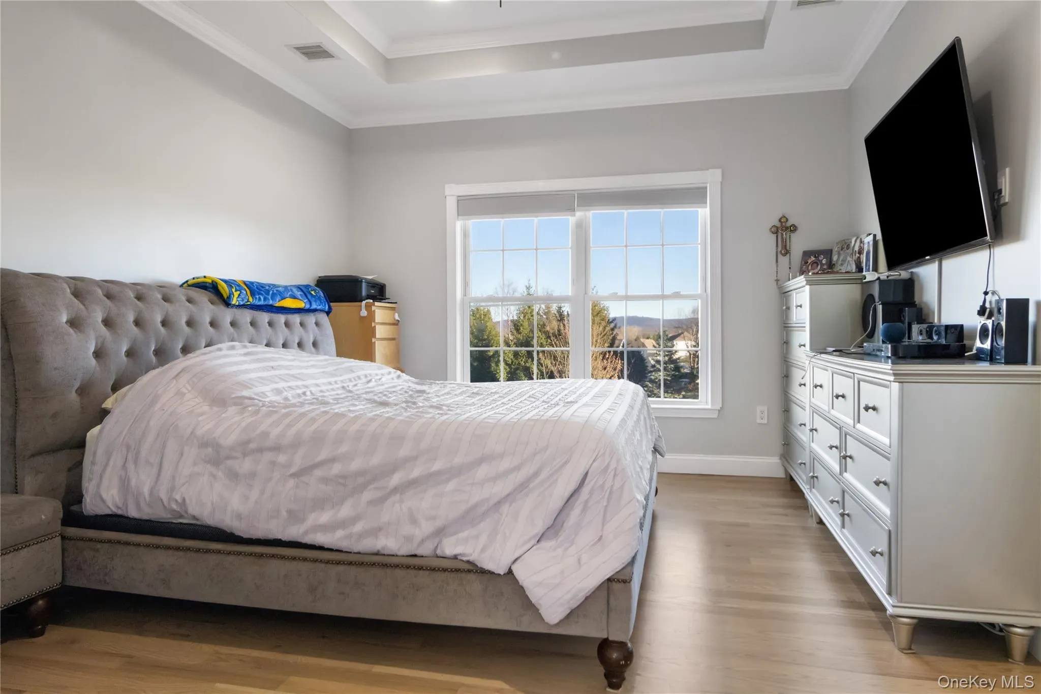Bedroom featuring light wood-style flooring, crown molding, and a tray ceiling Bedroom featuring light wood-style flooring, crown molding, and a tray ceiling