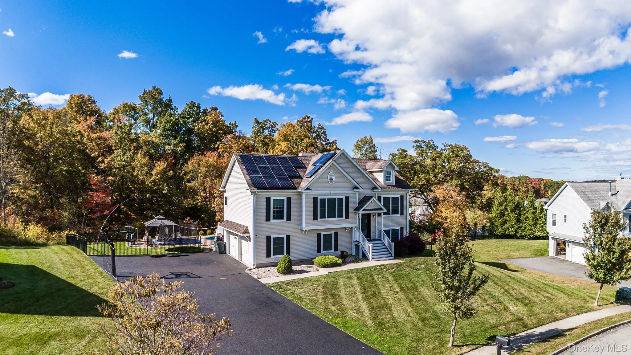 View of front facade featuring a front yard, an attached garage, driveway, and roof mounted solar panels View of front facade featuring a front yard, an attached garage, driveway, and roof mounted solar panels