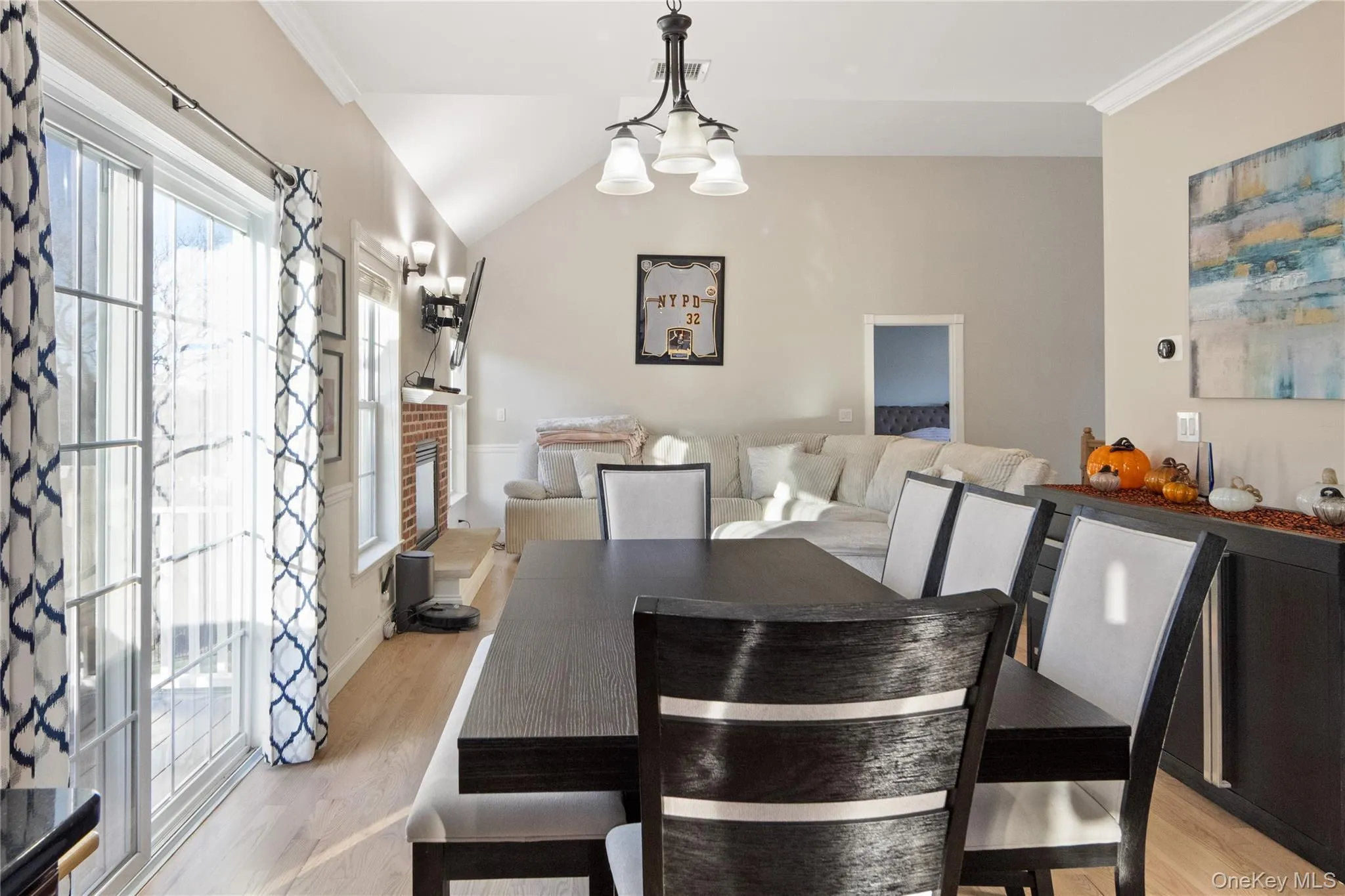 Dining space featuring lofted ceiling, a chandelier, a fireplace, light wood-style floors, and crown molding Dining space featuring lofted ceiling, a chandelier, a fireplace, light wood-style floors, and crown molding