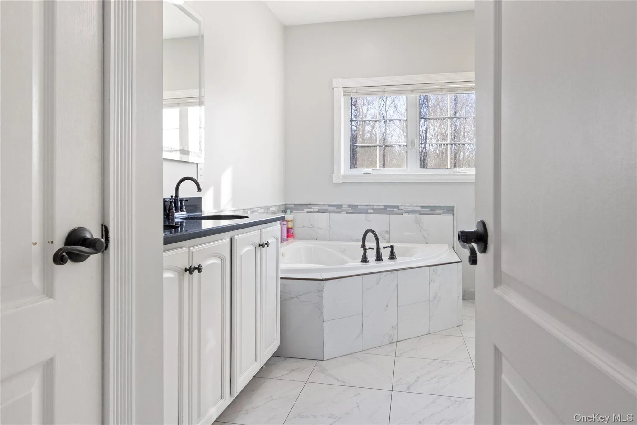 Full bathroom featuring a garden tub, vanity, light marble finish flooring, and healthy amount of natural light Full bathroom featuring a garden tub, vanity, light marble finish flooring, and healthy amount of natural light