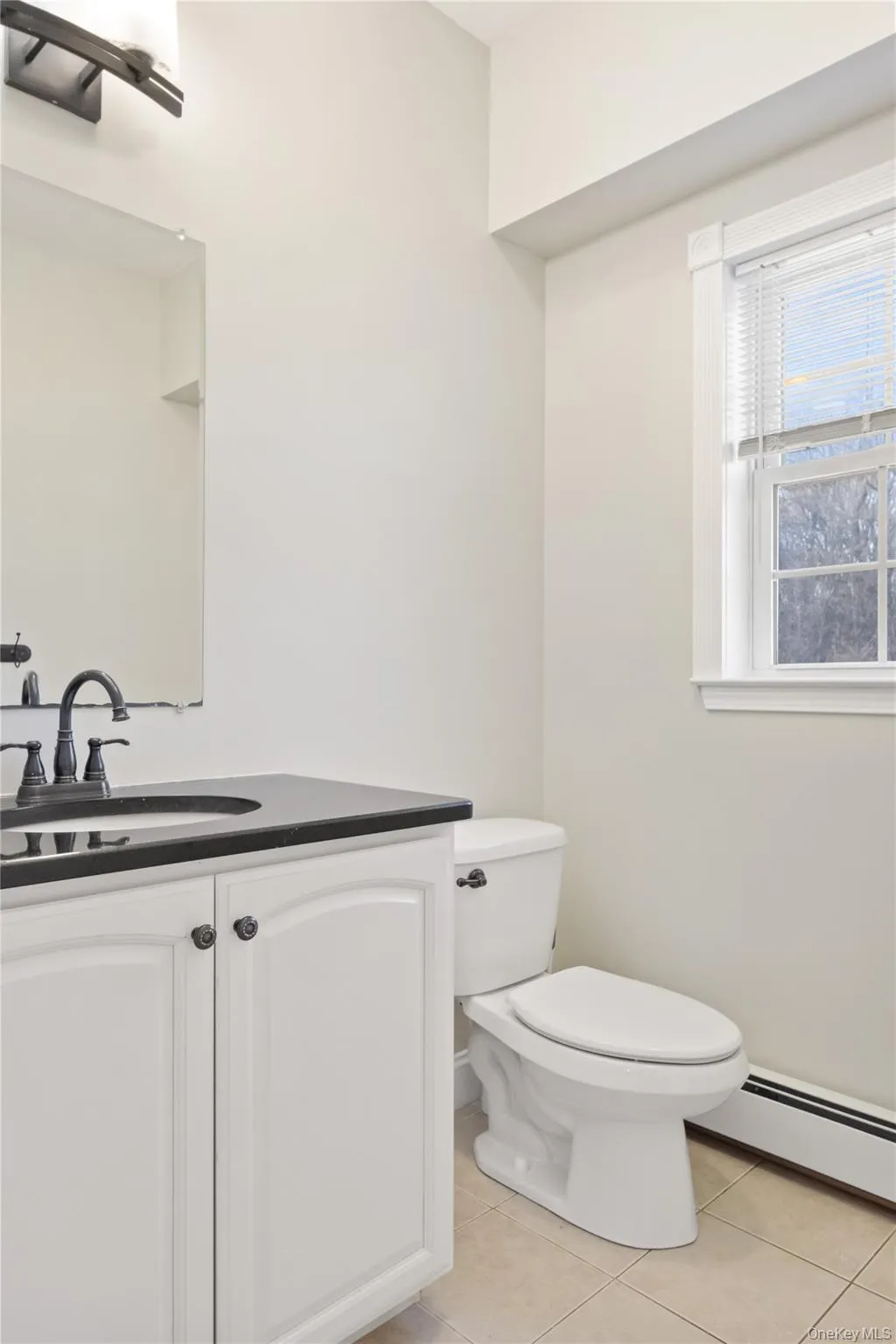 Half bathroom featuring baseboard heating, vanity, and light tile patterned floors Half bathroom featuring baseboard heating, vanity, and light tile patterned floors